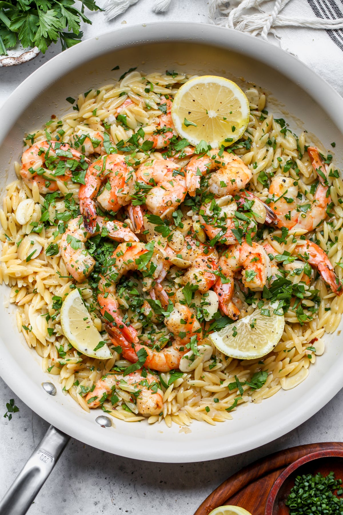 A white skillet filled with orzo, shrimp, lemon wedges, and herbs.