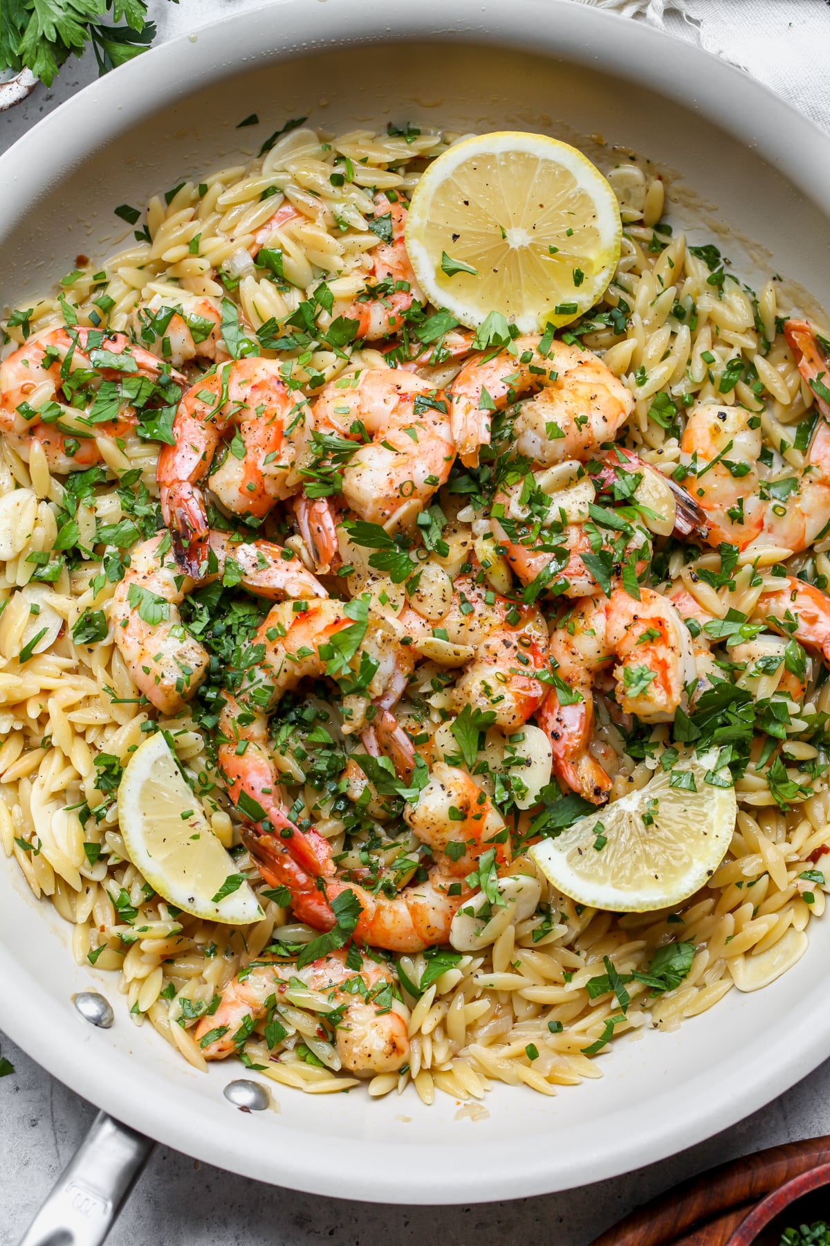 Shrimp scampi orzo styled in a white skillet with lemon wedges as garnish.