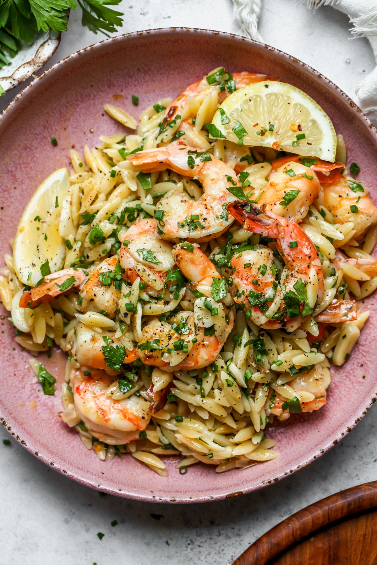 Shrimp scampi orzo styled in a pink serving bowl topped with herbs and lemon wedges.