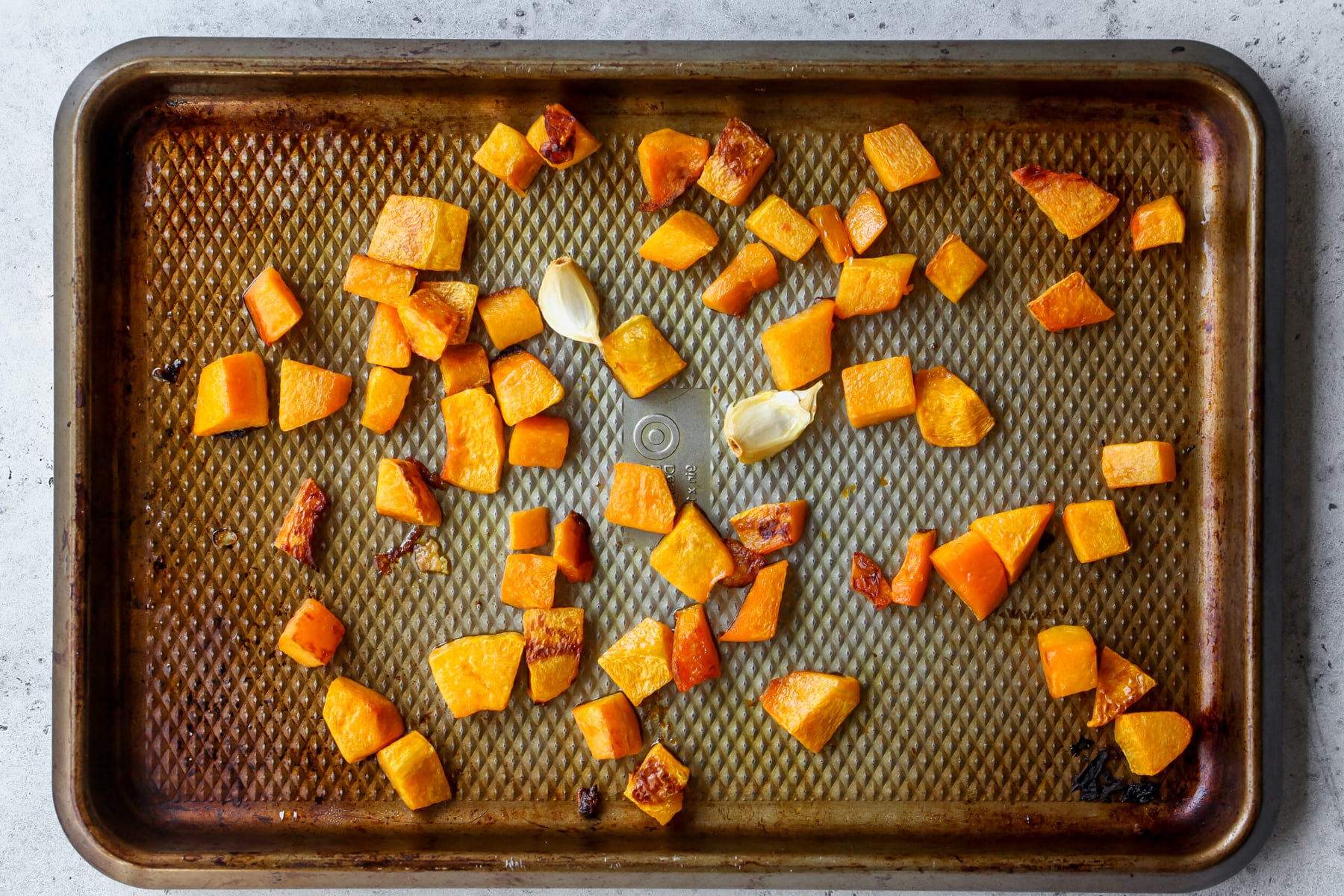 Cubes of butternut squash and garlic being roasted on a sheet pan.
