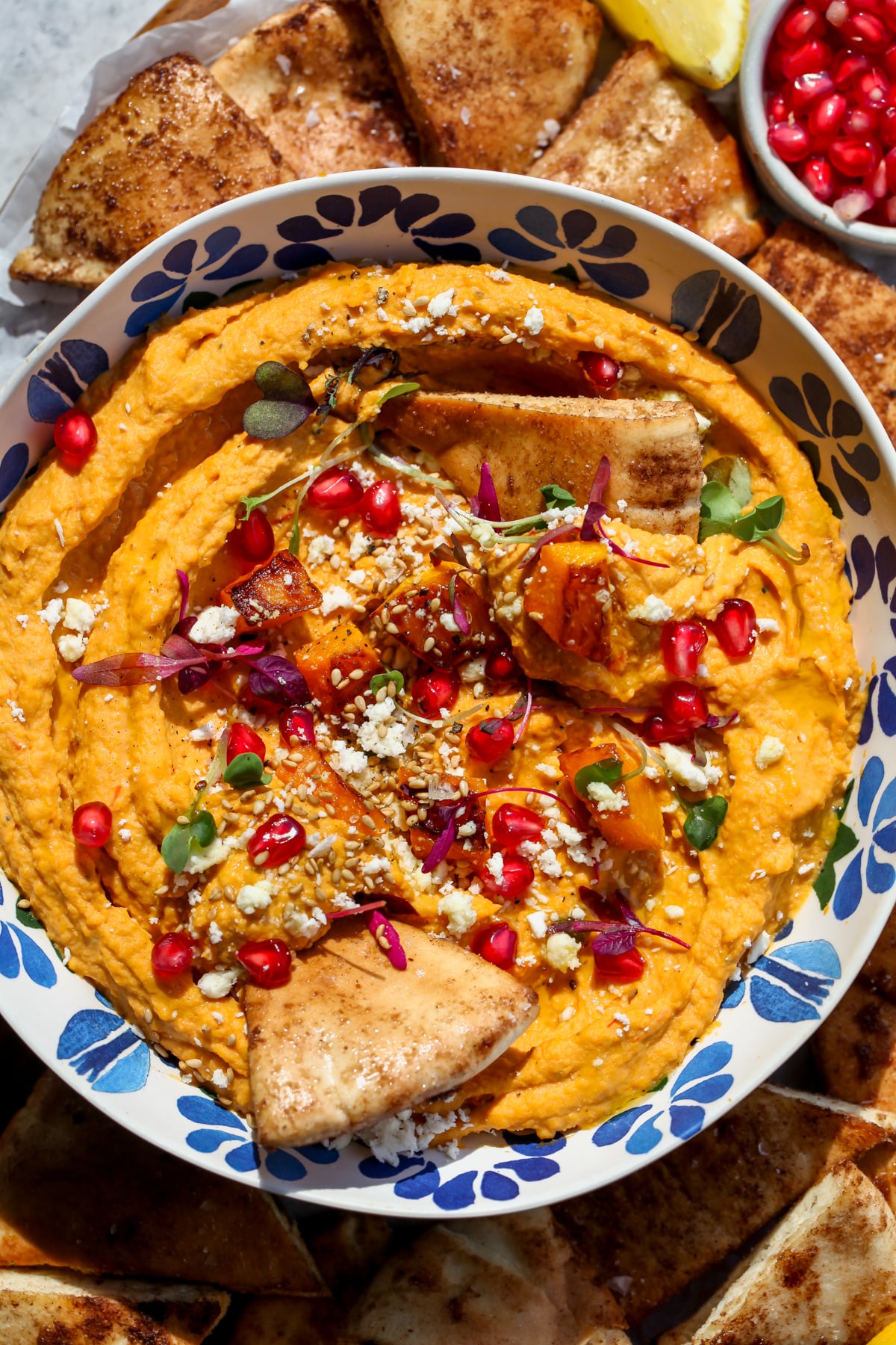 Butternut squash hummus styled in a blue floral bowl with cinnamon-sugar pita being dipped.