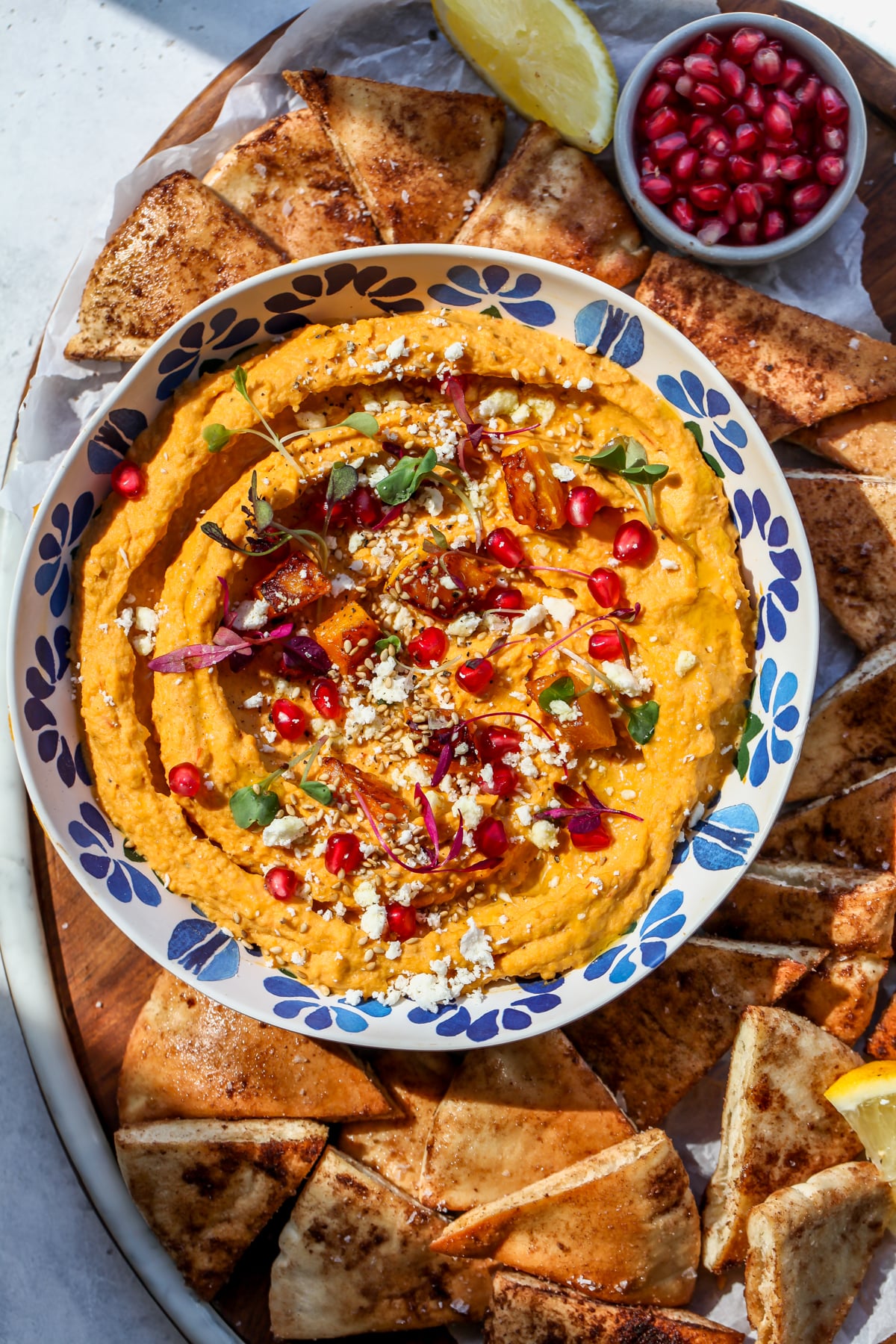 Butternut squash hummus being served in a blue bowl on a platter of pita chips.