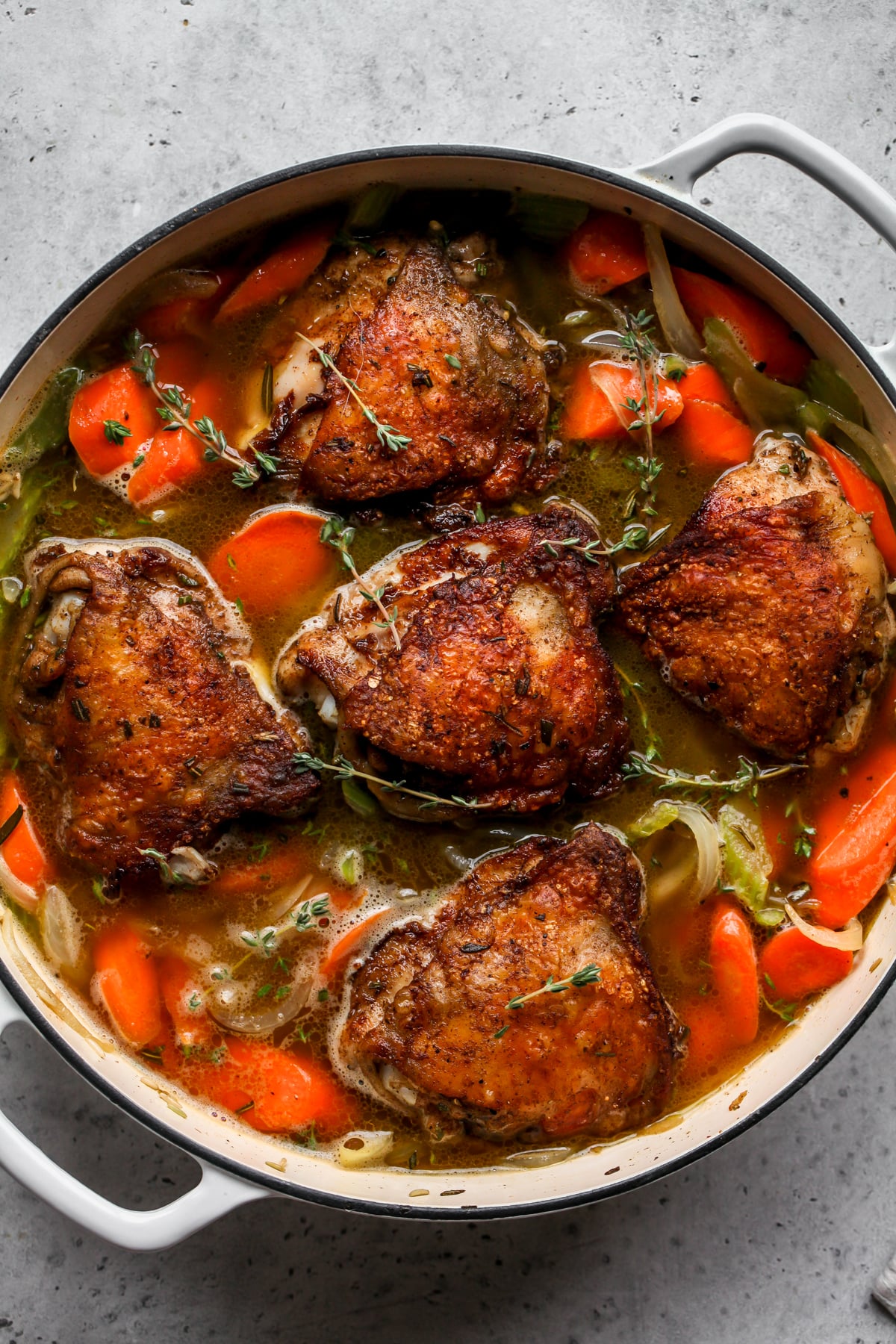 Chicken thighs being nestled back into skillet with veggies, wild rice, and broth.