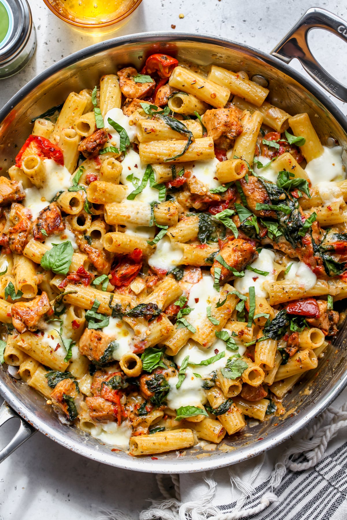 Pesto Chicken Pasta Bake topped with mozzarella and fresh basil styled in a stainless steel pan.