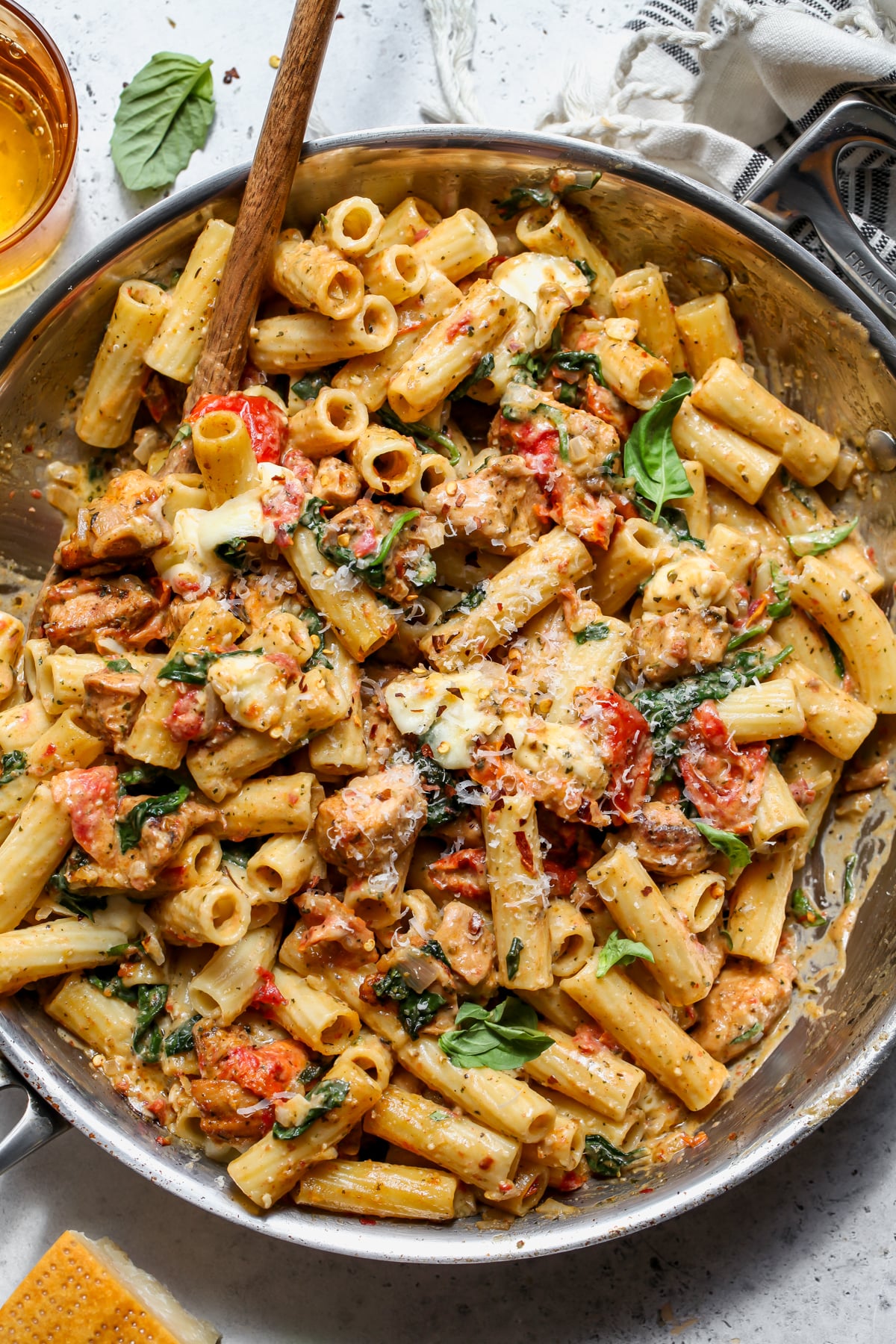 Pesto Chicken Pasta Bake in a large skillet with a wooden spoon resting on the left side.