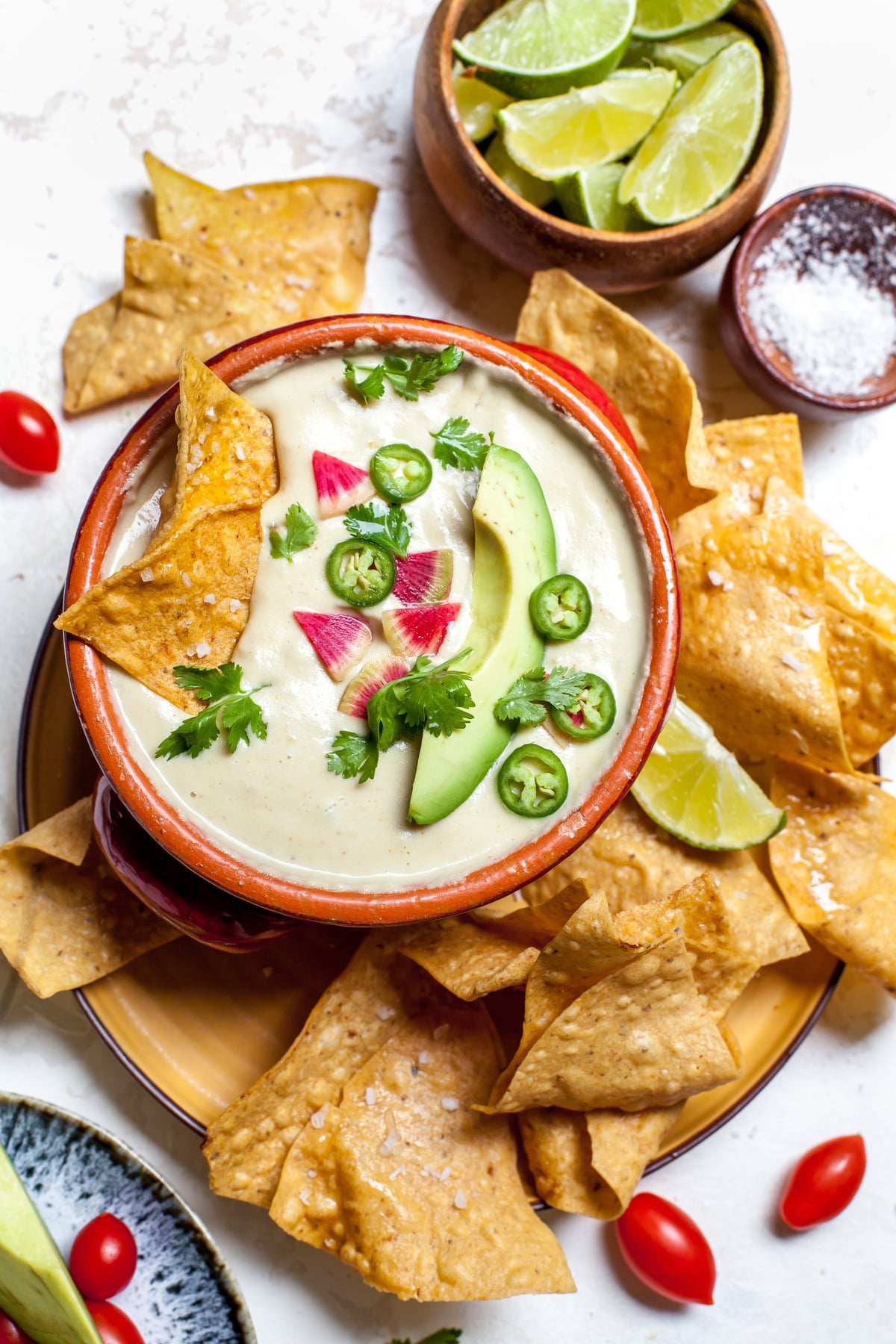 Vegan queso styled in a red bowl on a plate of tortilla chips.