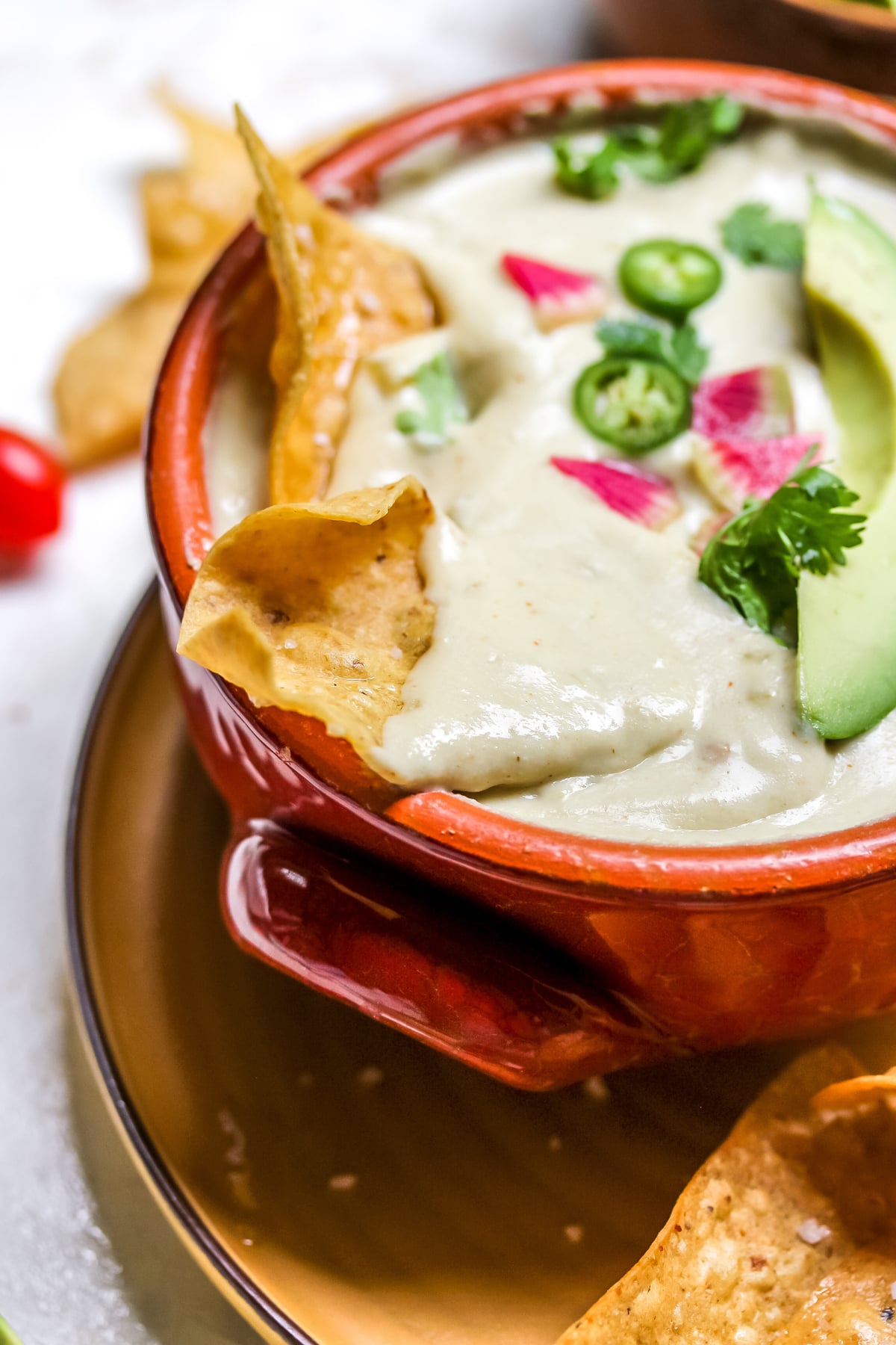 A chip being dipped into a red bowl filled with vegan queso.