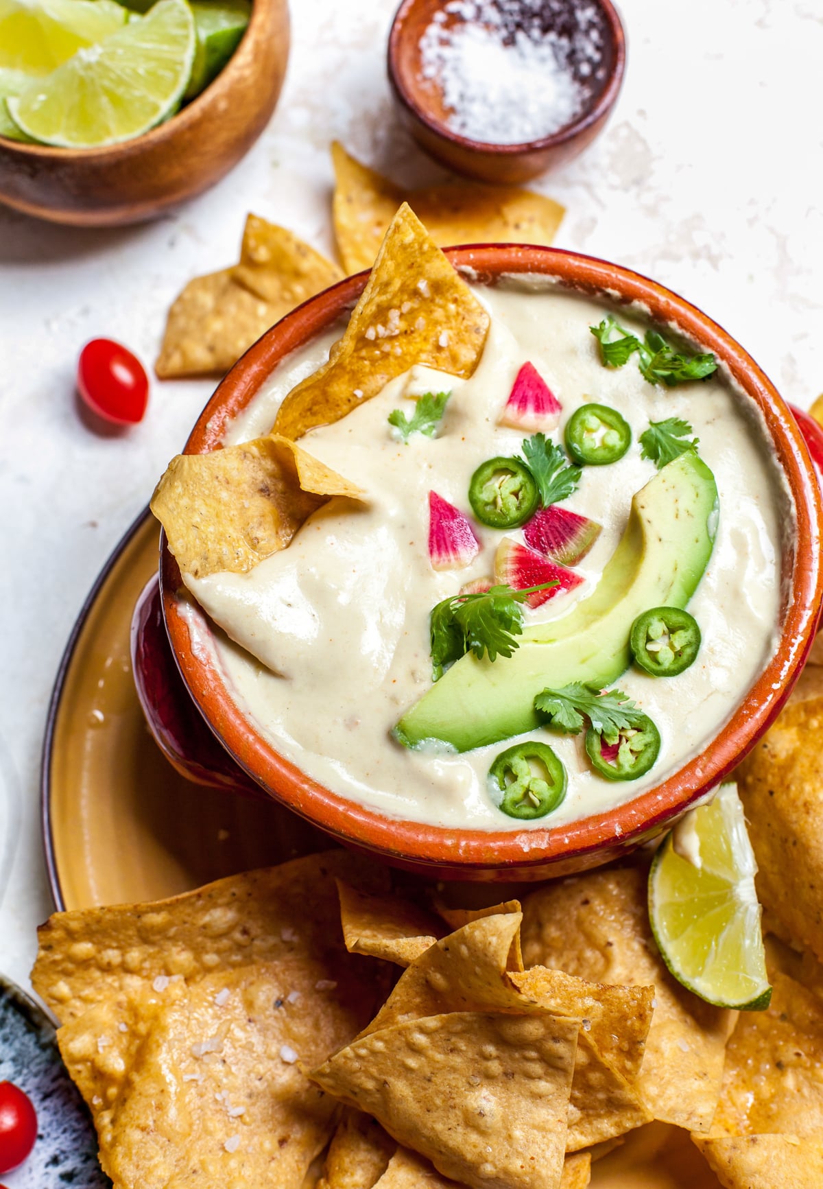 Vegan queso styled in a red bowl on top of a plate filled with tortilla chips.