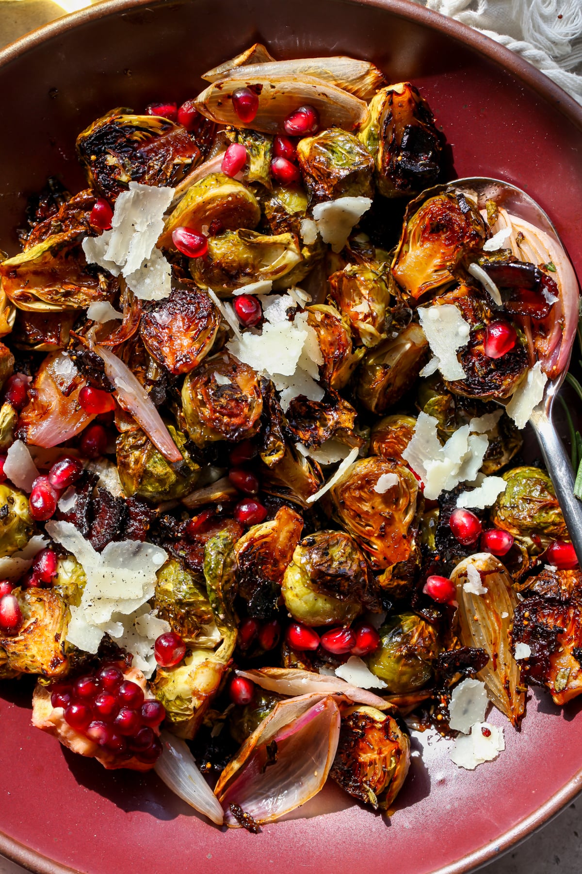 Balsamic glazed Brussels sprouts with bacon and shallots styled in a maroon serving bowl.