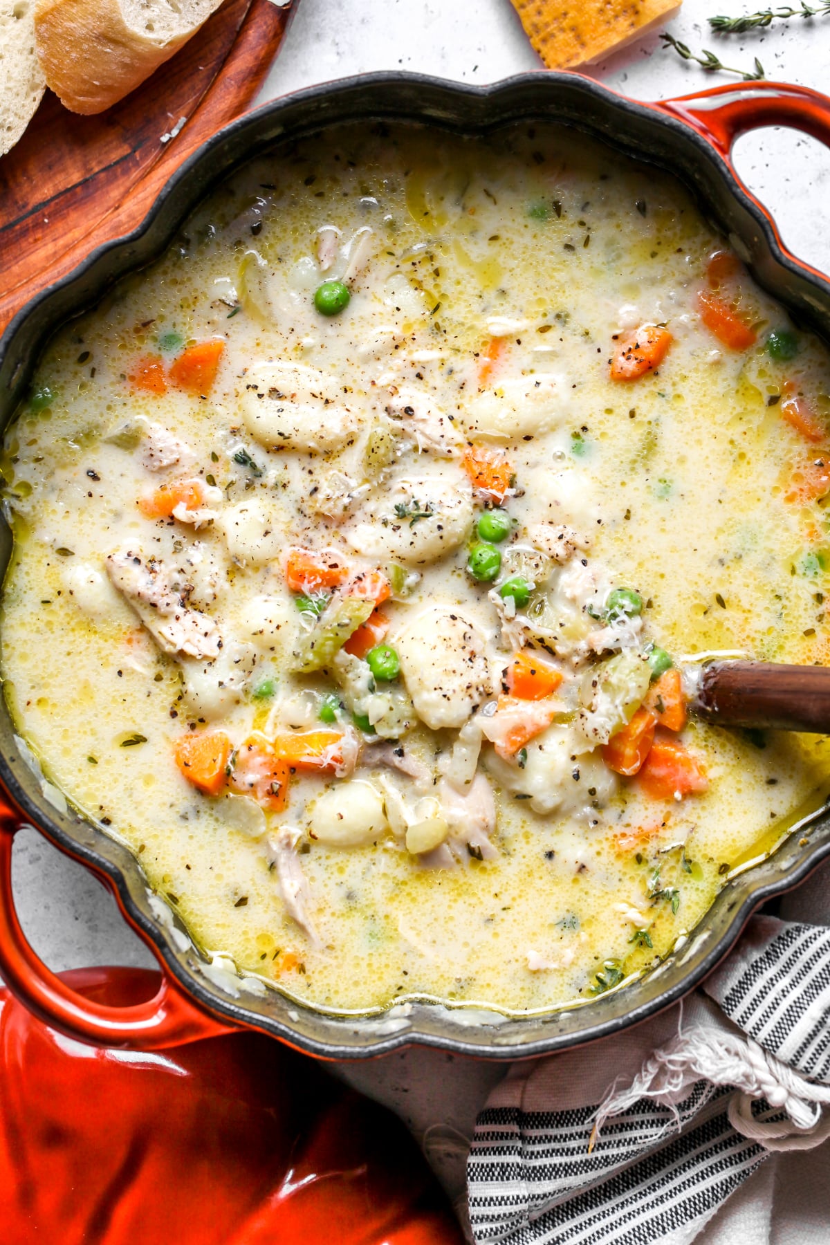 An orange pot filled with chicken gnocchi soup. Ladle resting on the right side.