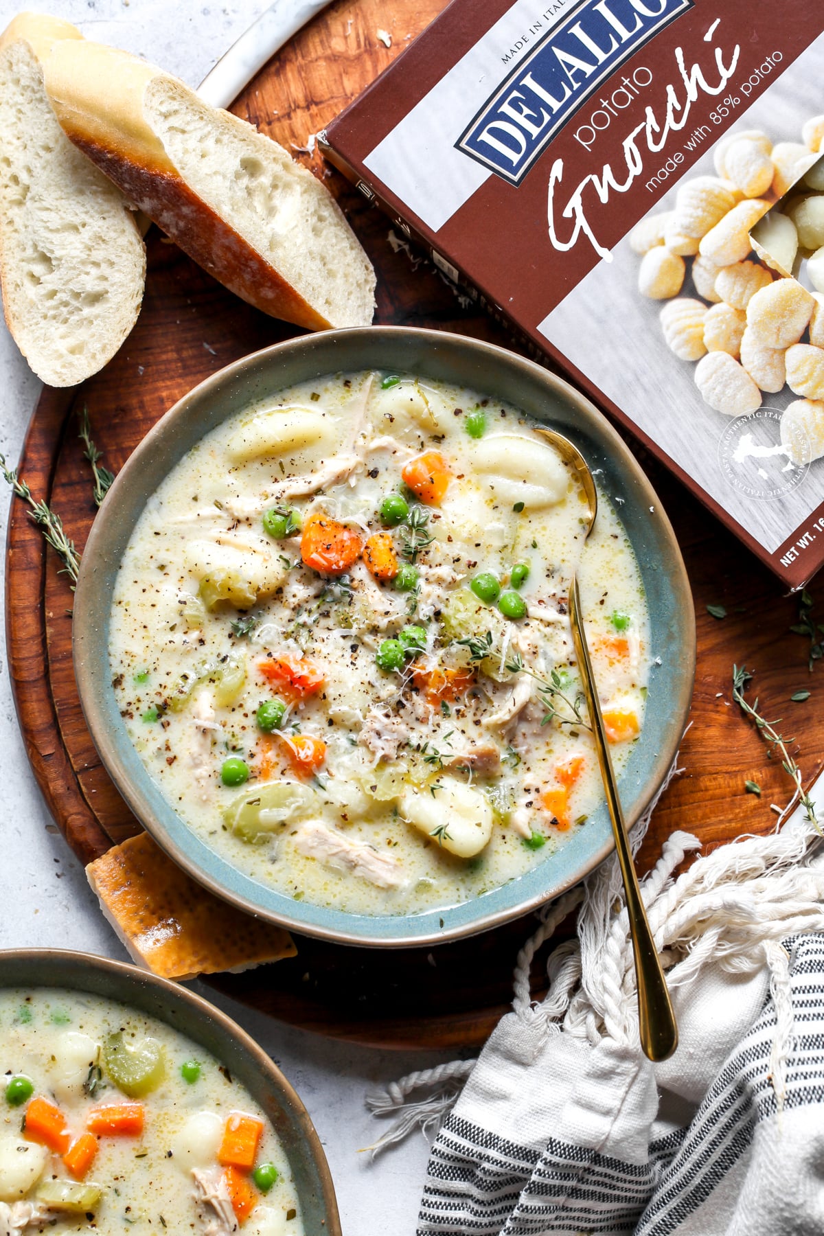 A bowl of chicken gnocchi soup next to a package of DeLallo potato gnocchi on a wooden surface.