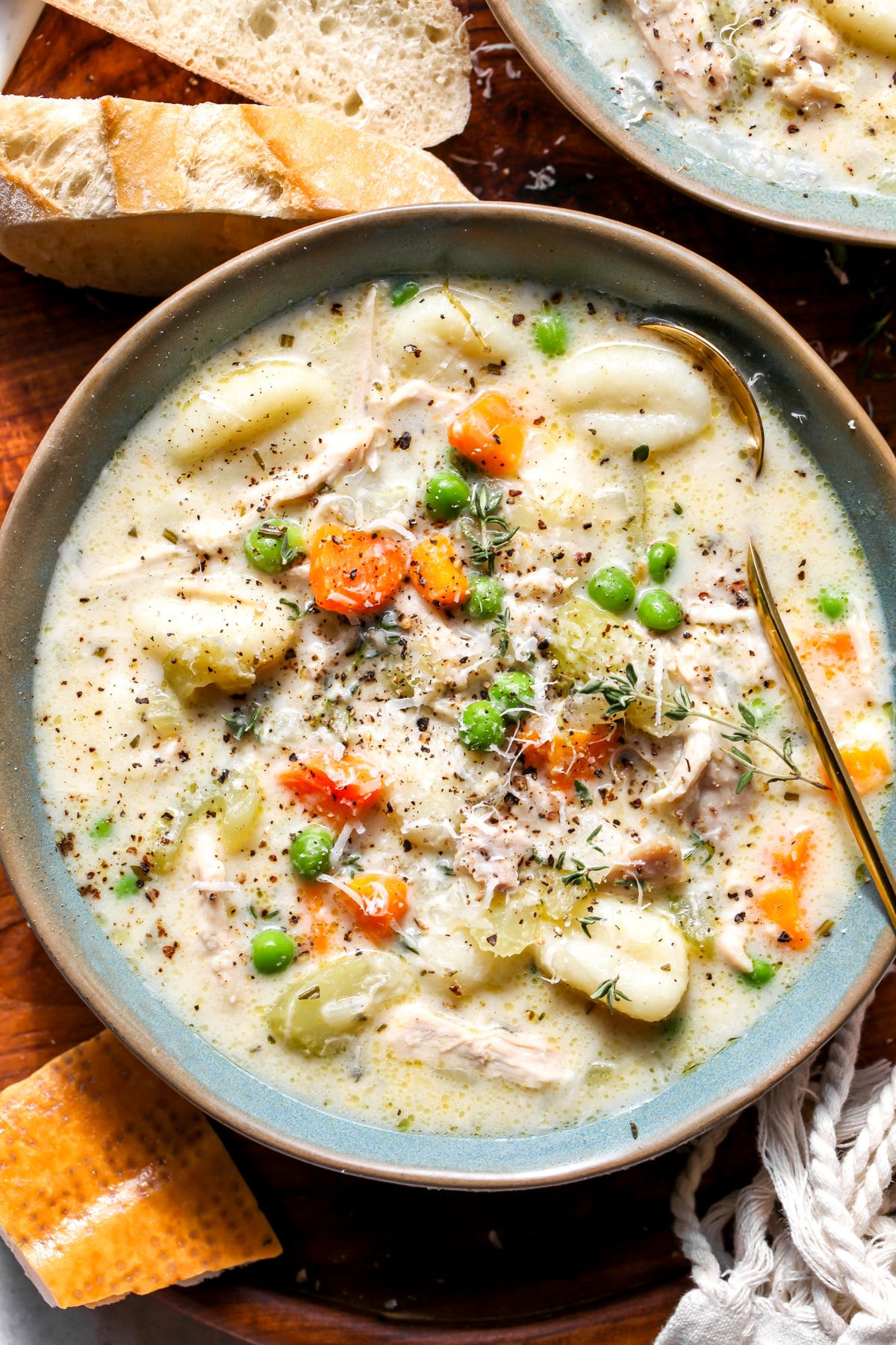A close up view of chicken and gnocchi soup styled in a blue bowl topped with Parmesan and fresh thyme.