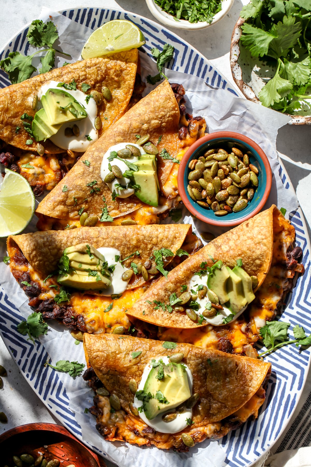 Crispy Chipotle Black Bean Pumpkin Tacos arranged on a blue and white platter topped with sour cream, avocado, and pumpkin seeds.