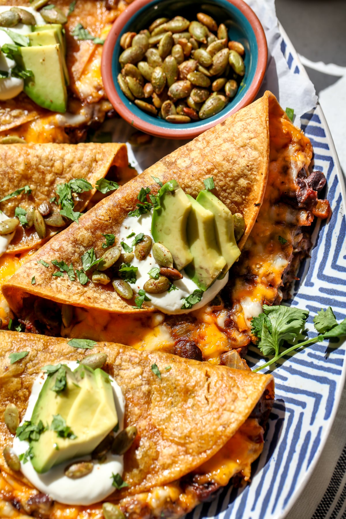 Black bean pumpkin tacos arranged on a serving platter topped with sour cream, avocado slices, and pumpkin seeds.