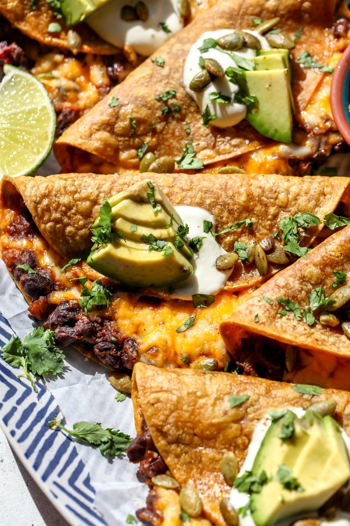 Crispy chipotle black bean pumpkin tacos arranged on a platter showing gooey insides.