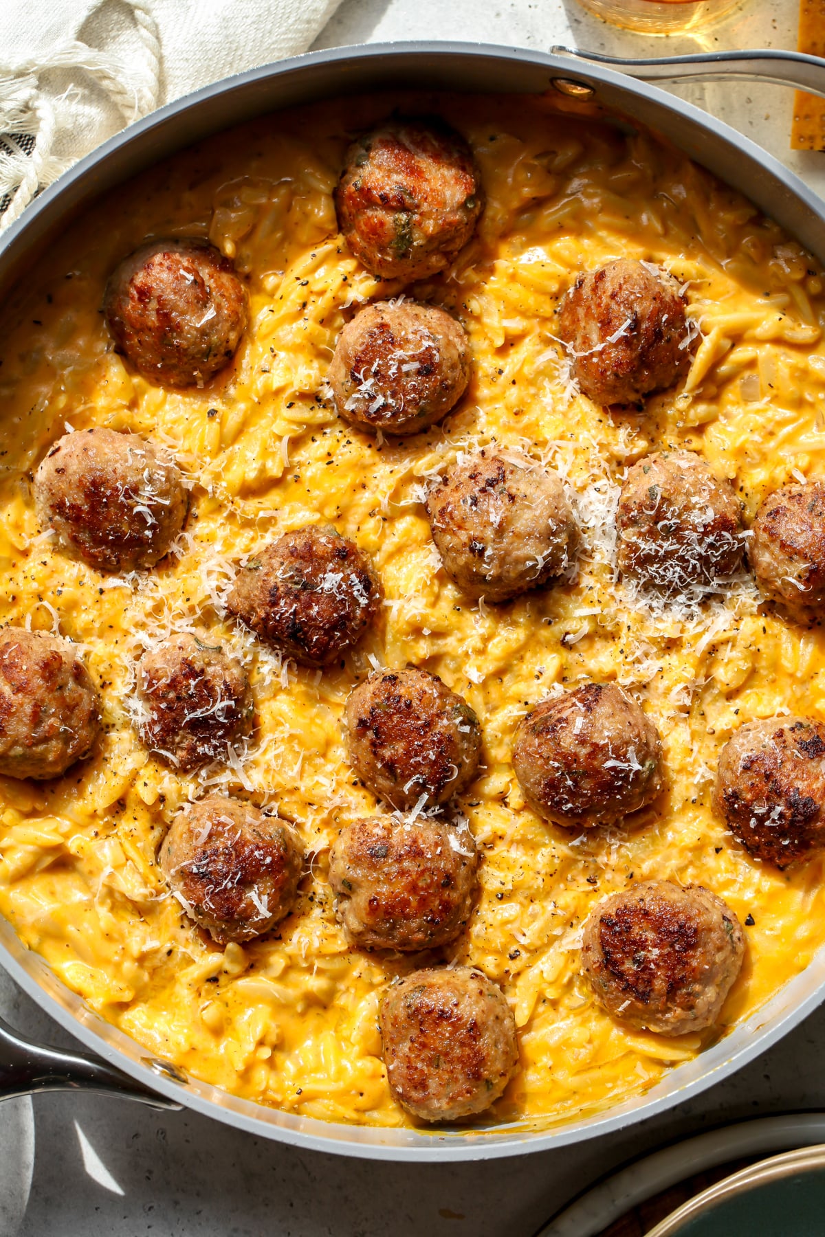 Sage turkey meatballs arranged in a skillet of pumpkin orzo topped with Parmesan.