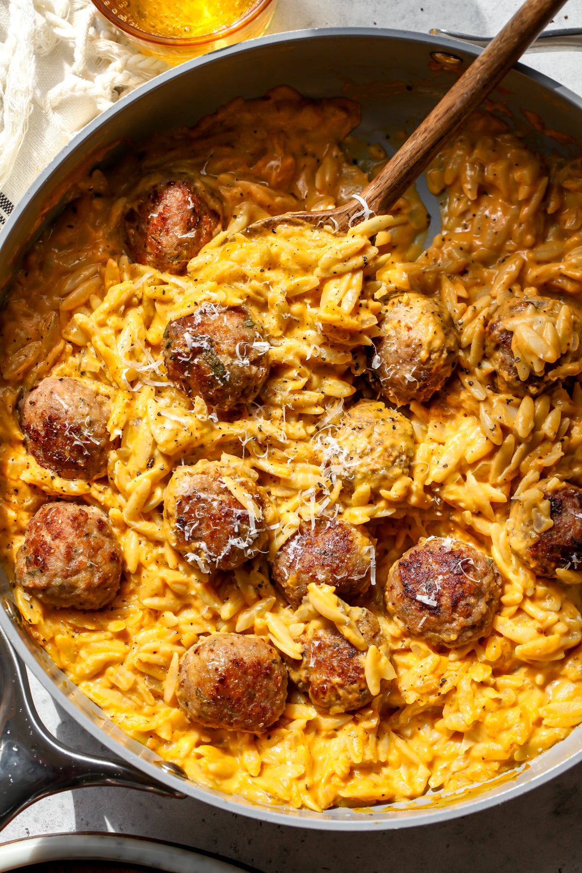 A wooden spoon stirring a pot of pumpkin orzo with turkey meatballs.