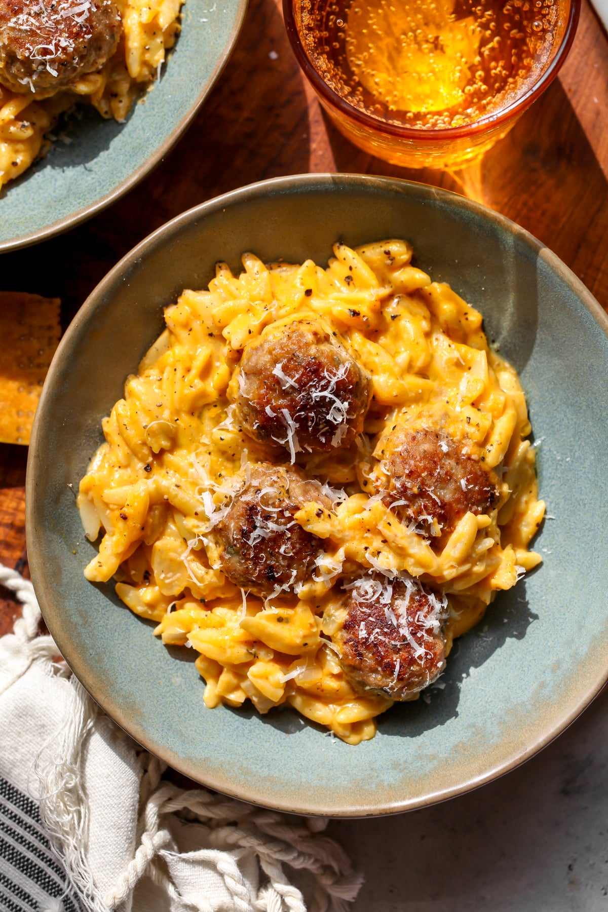 A blue bowl filled with pumpkin orzo and four sage turkey meatballs.
