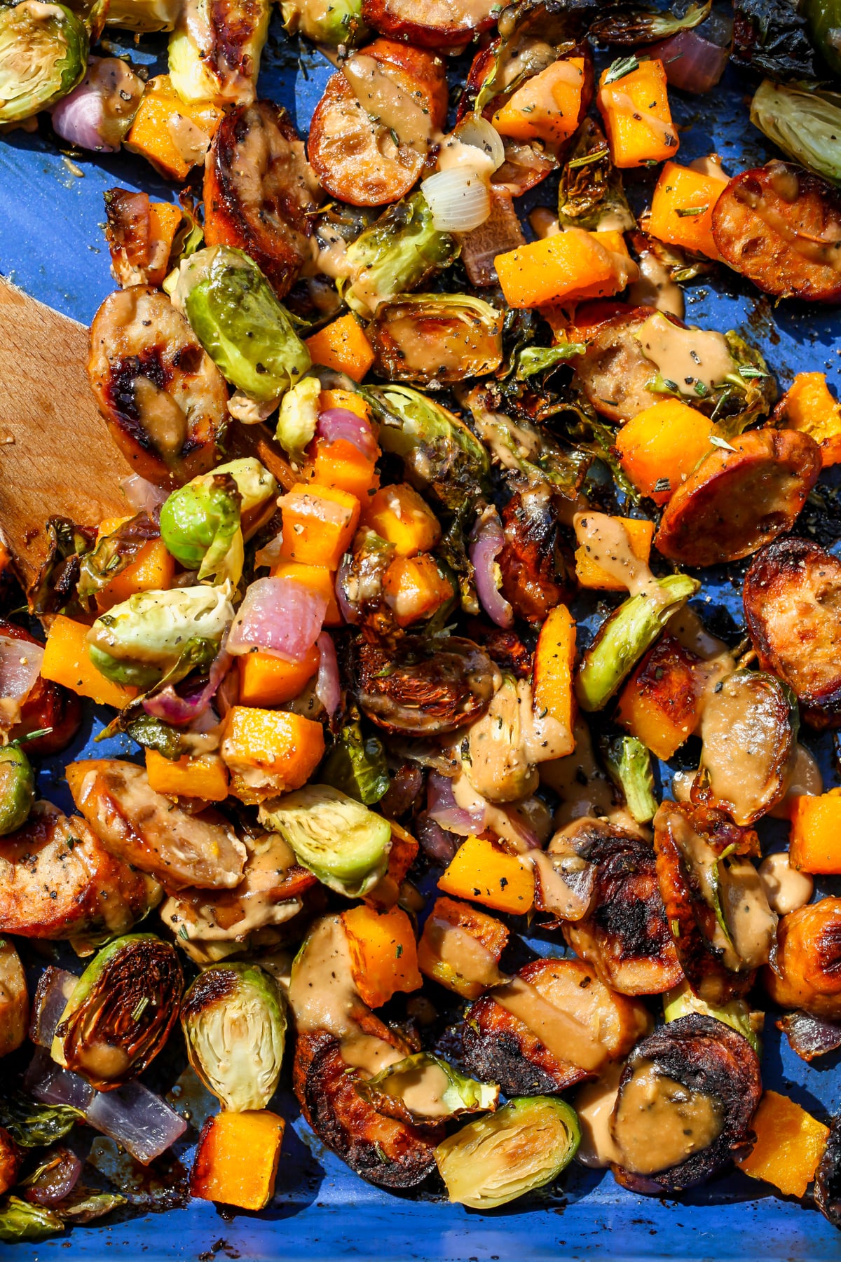 Sheet pan chicken sausage and veggies being tossed on a blue rimmed baking sheet.