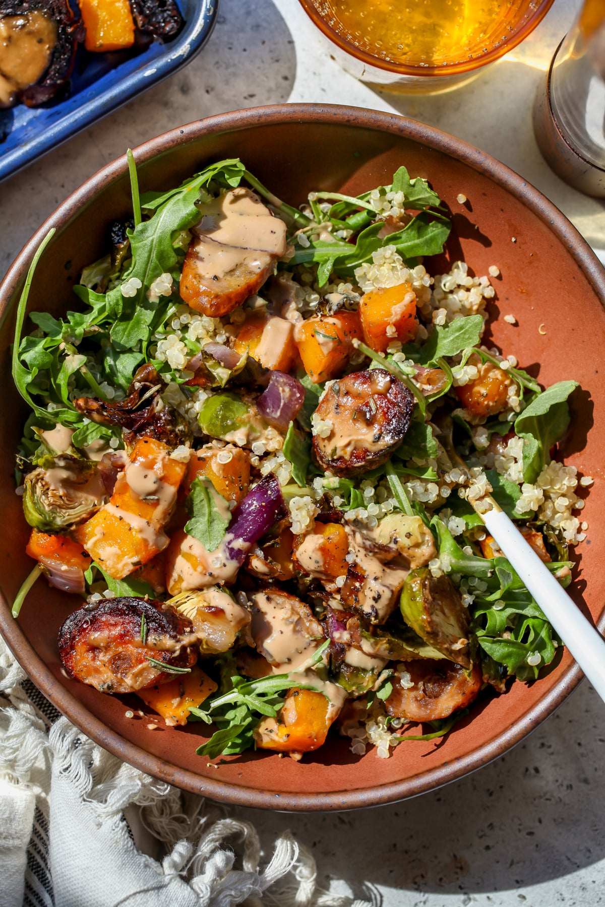 Chicken sausage and veggie mixture served over quinoa and arugula in a maroon bowl.
