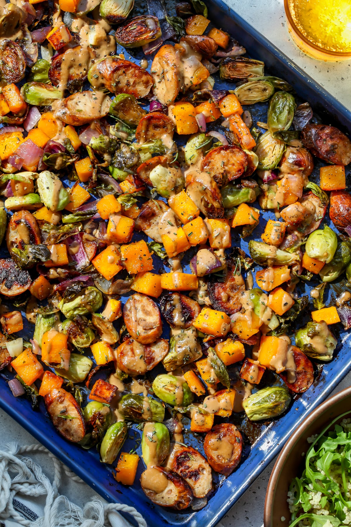 Sheet pan chicken sausage and veggies styled on a large rimmed blue baking sheet.