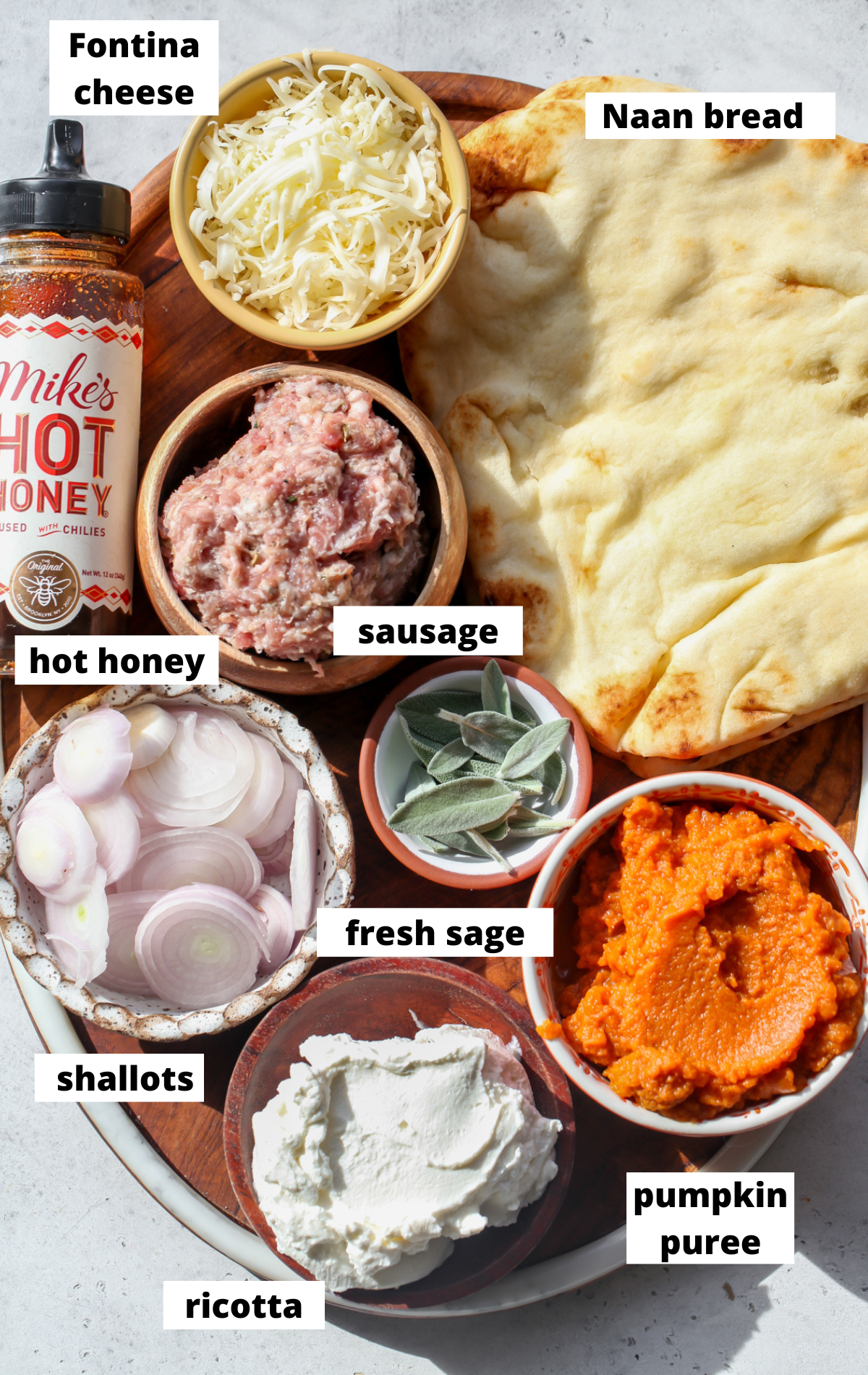Recipe ingredients in separate bowls arranged on a wooden platter with labels.