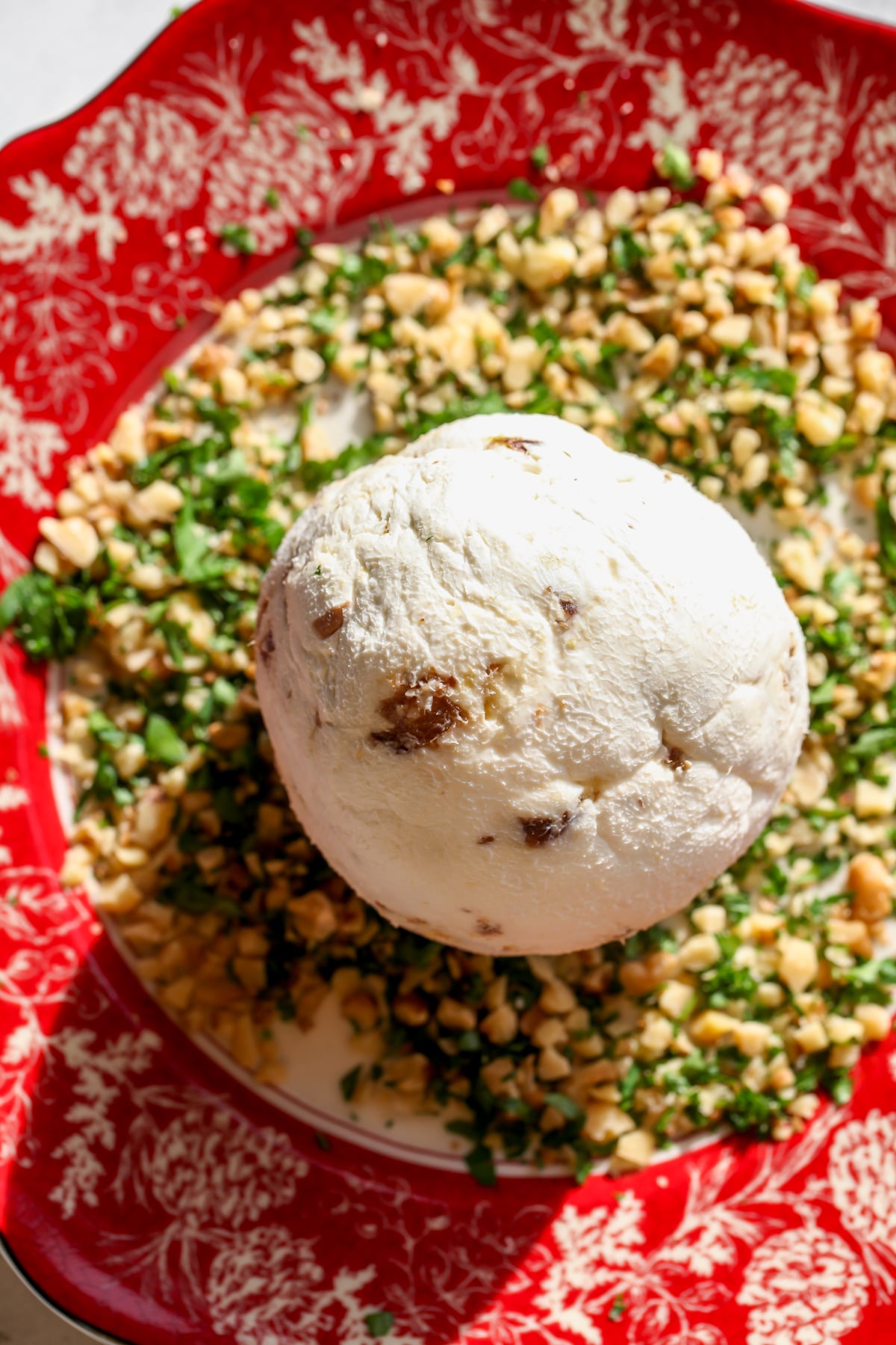 Cream cheese, goat cheese, dates, and lemon zest rolled into a ball and placed on a plate with chopped parsley and walnuts.