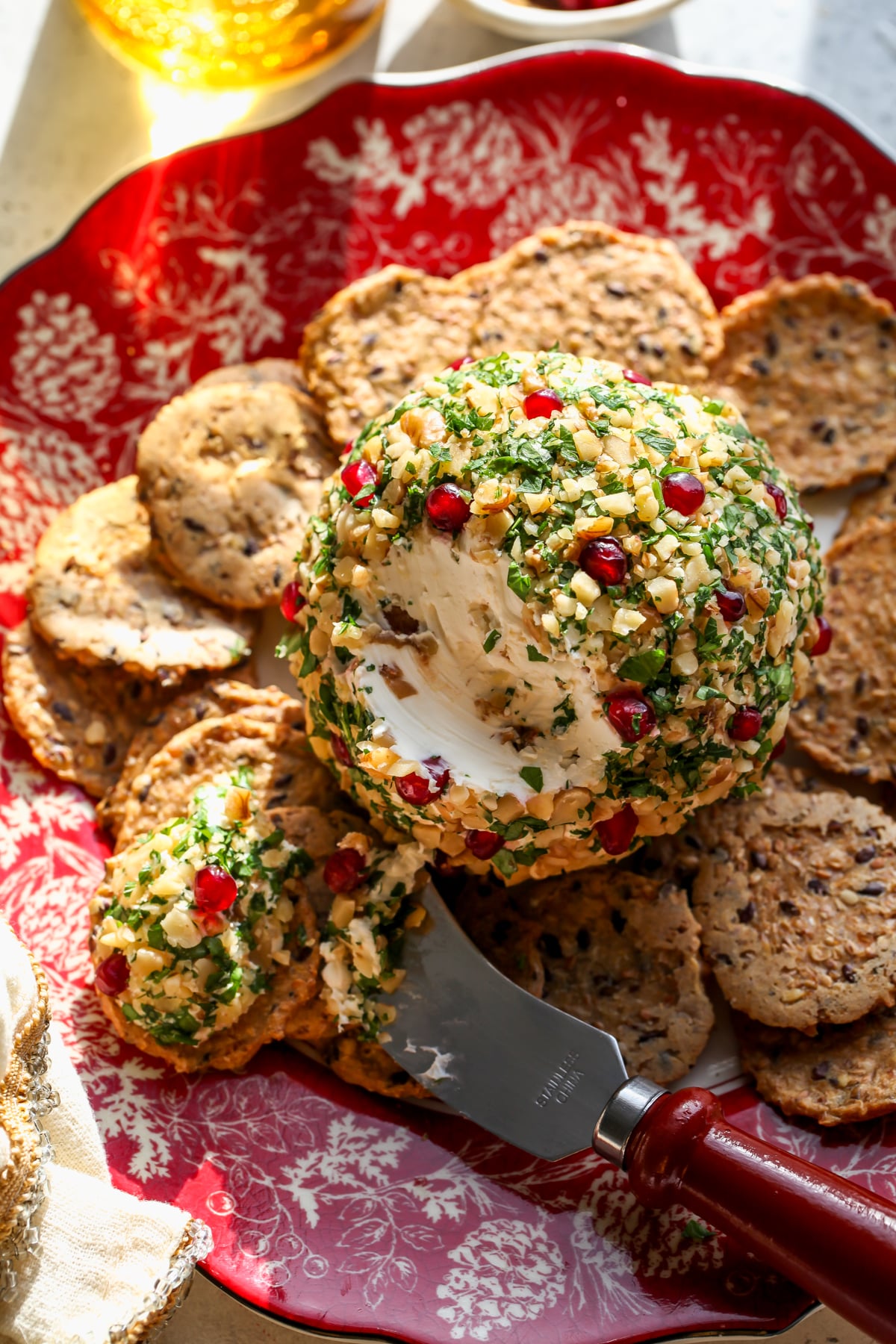 Cheese ball recipe topped with walnuts and parsley assembled on a red and white plate.