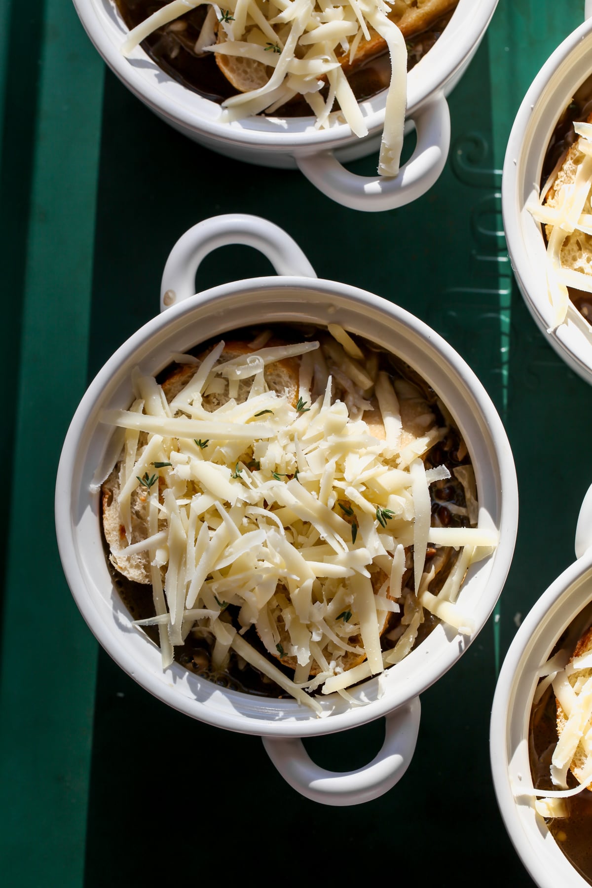 Mini oven-safe bowls of soup being topped with baguette and Gruyere cheese.