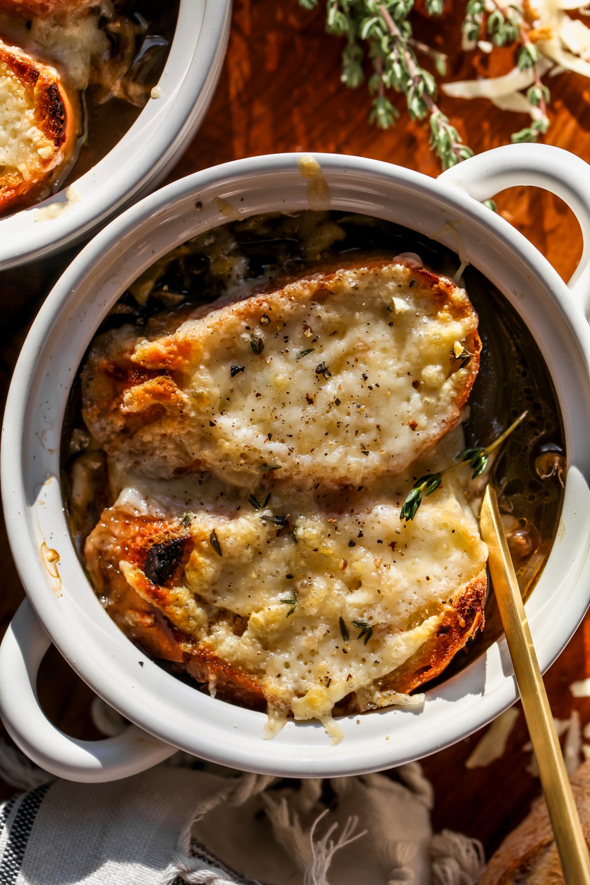 A bowl of French Onion Lentil Soup topped with baguette and Gruyere in a white bowl.