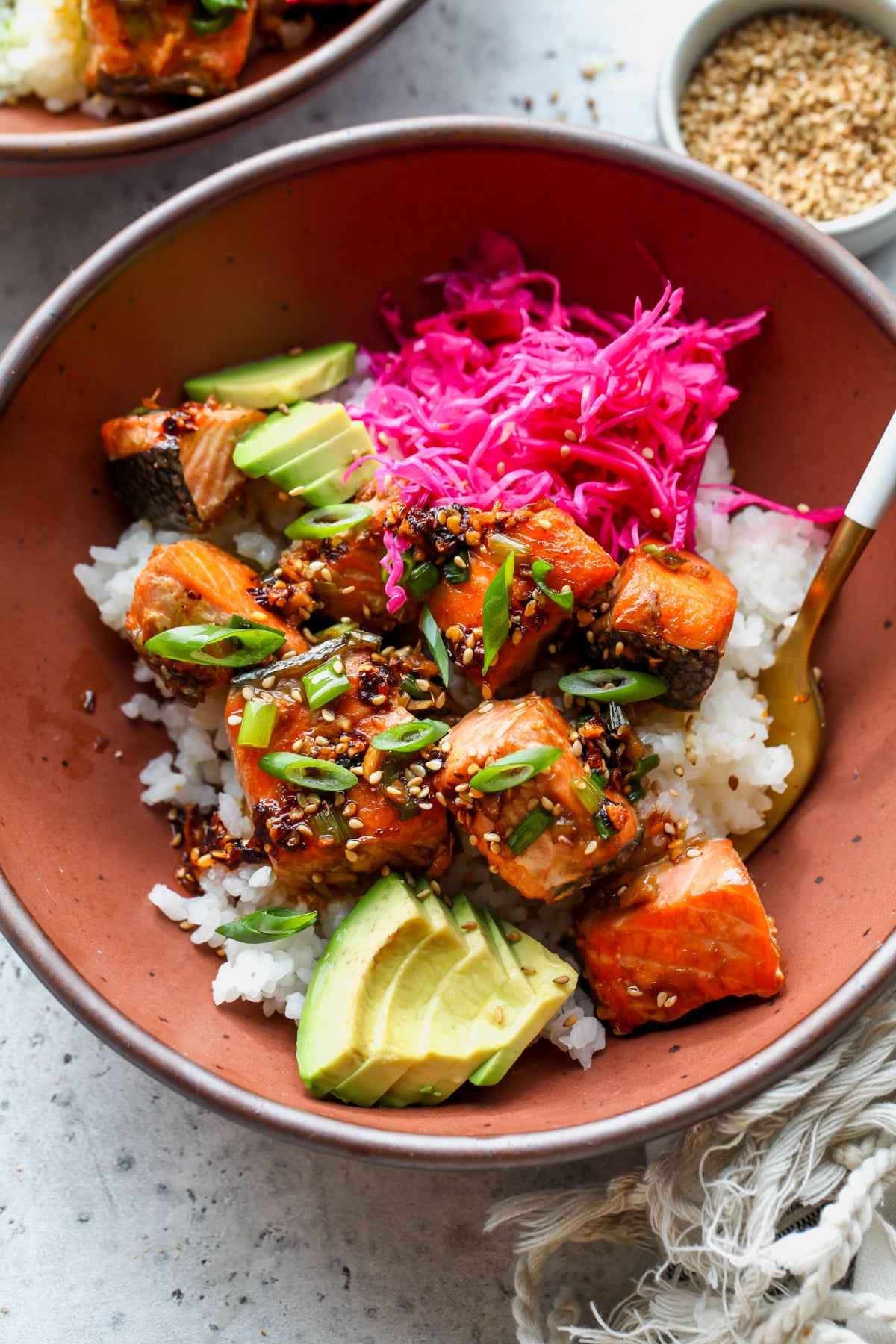 Salmon, cabbage, and avocado styled over sushi rice in a maroon bowl.