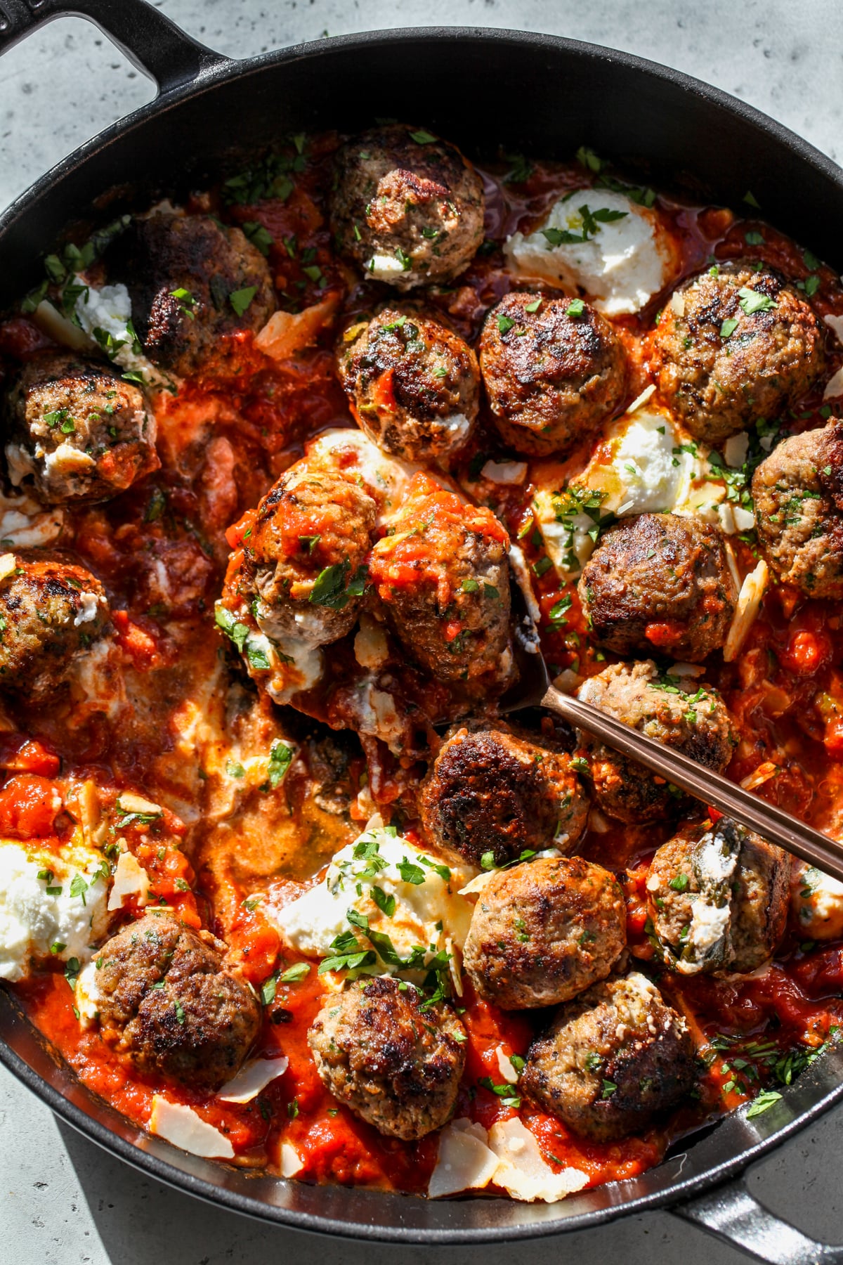 A spoon scooping up a portion of ricotta meatballs in tomato-basil sauce.
