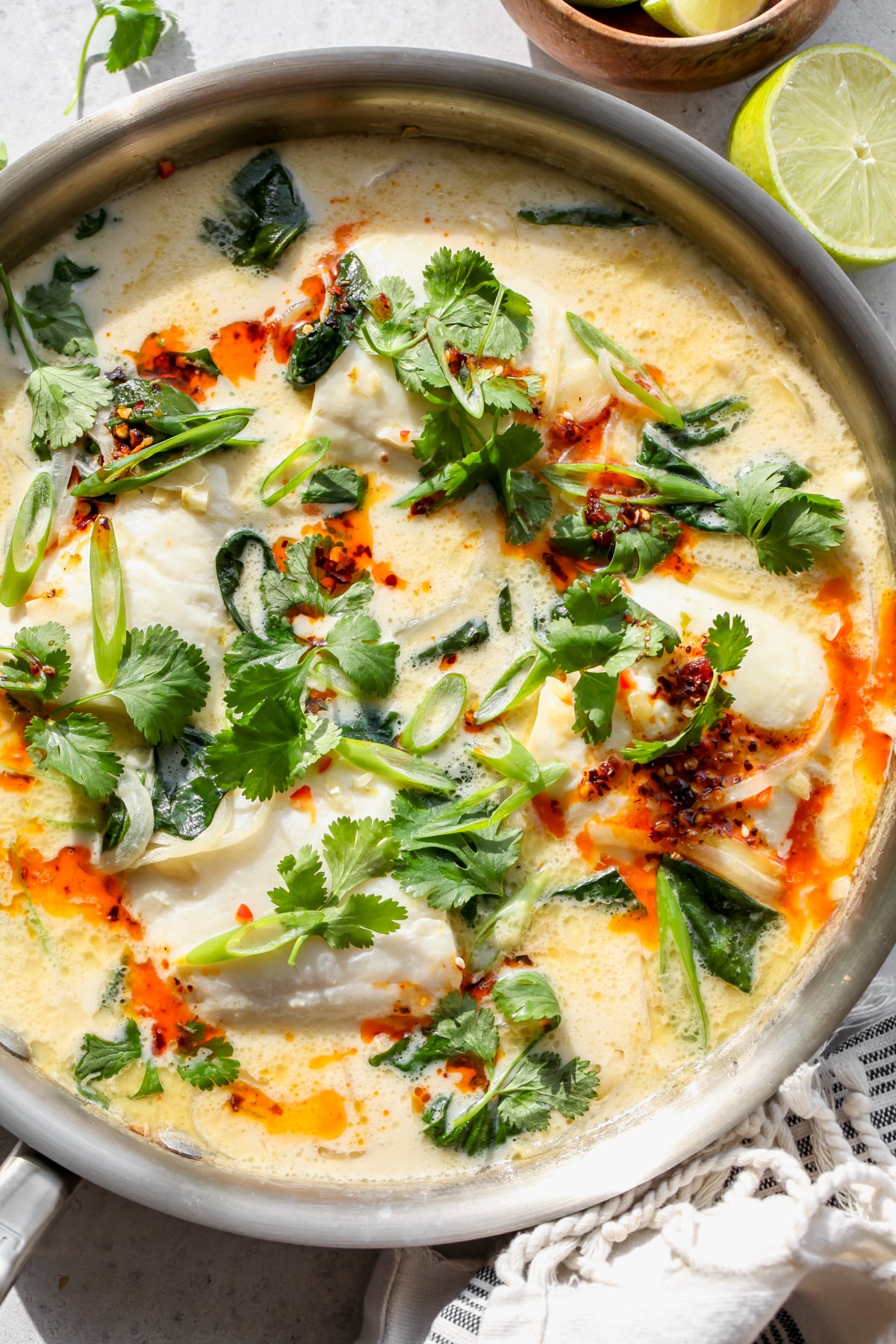Coconut Poached Fish styled in a large skillet topped with cilantro, scallions, and chili oil.