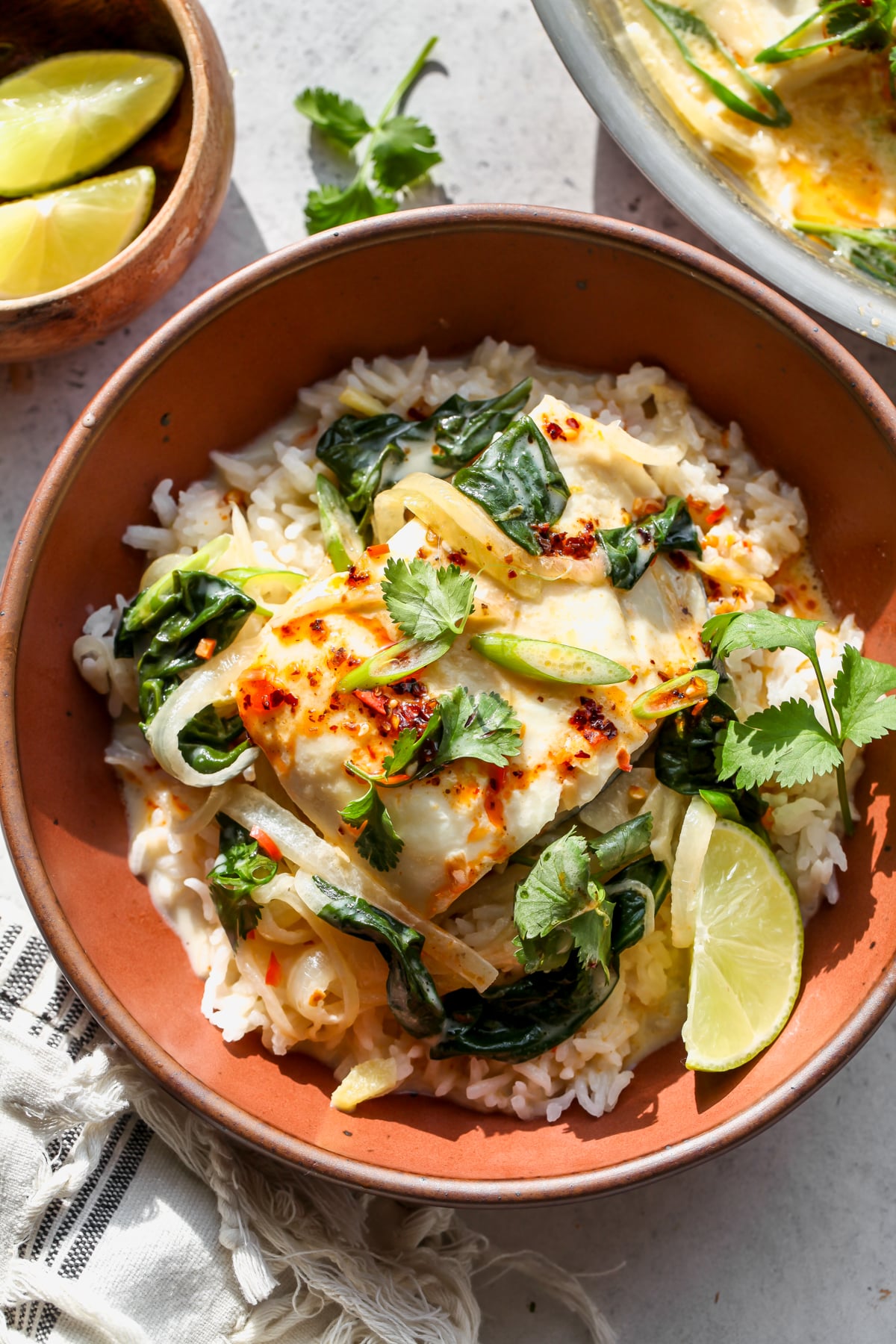 Coconut poached fish and broth being served over Jasmine rice in a maroon bowl. Topped with cilantro, scallions, and chili oil.