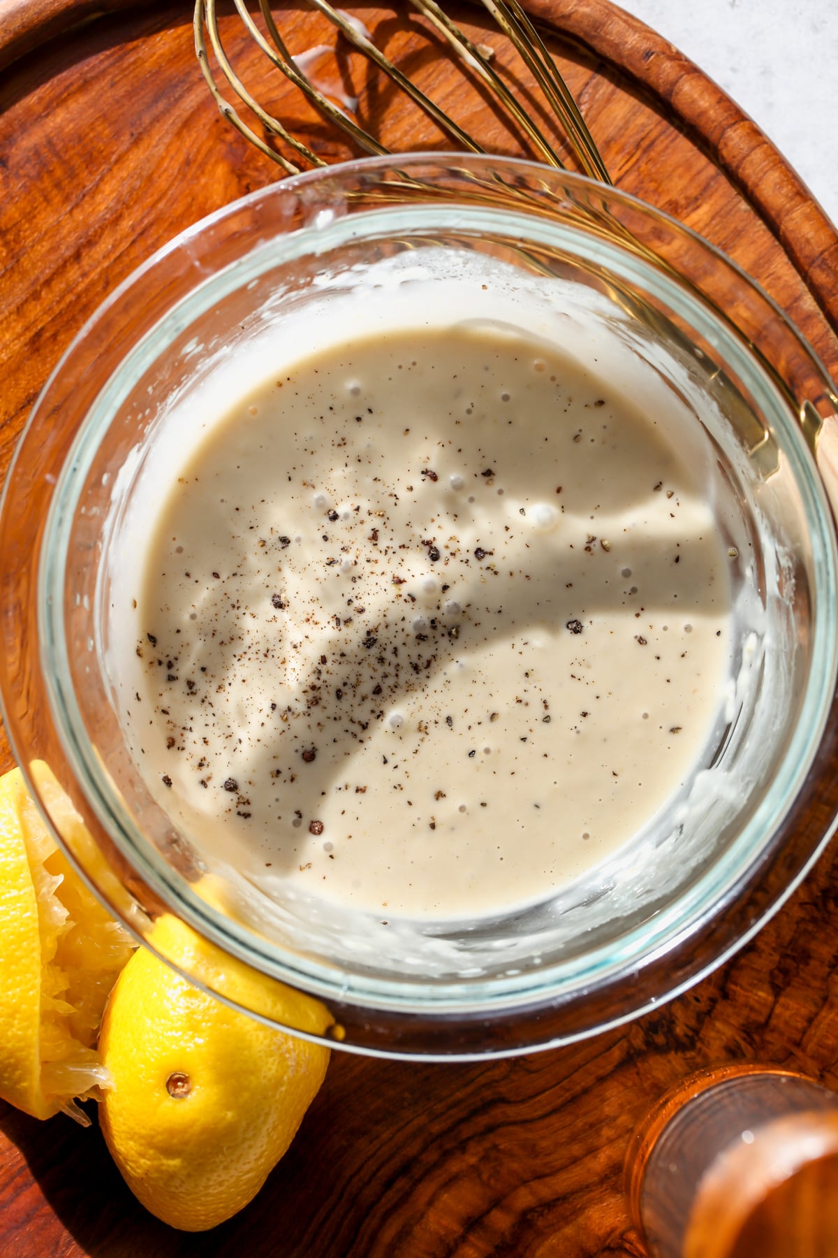 Miso Caesar dressing with cracked black pepper in a small clear glass mixing bowl.