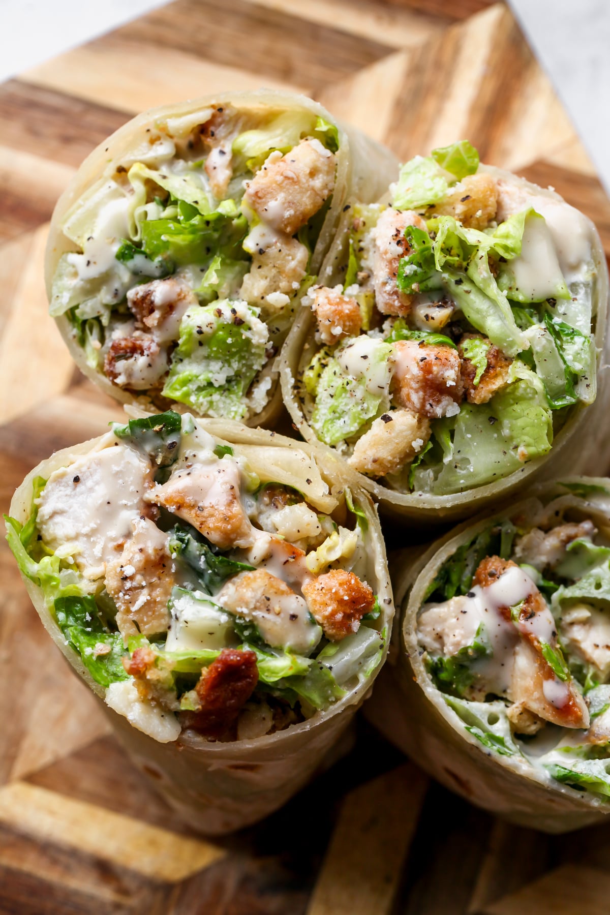 Two Miso Chicken Caesar Wraps sliced in half and assembled next to one another on a wooden cutting board.