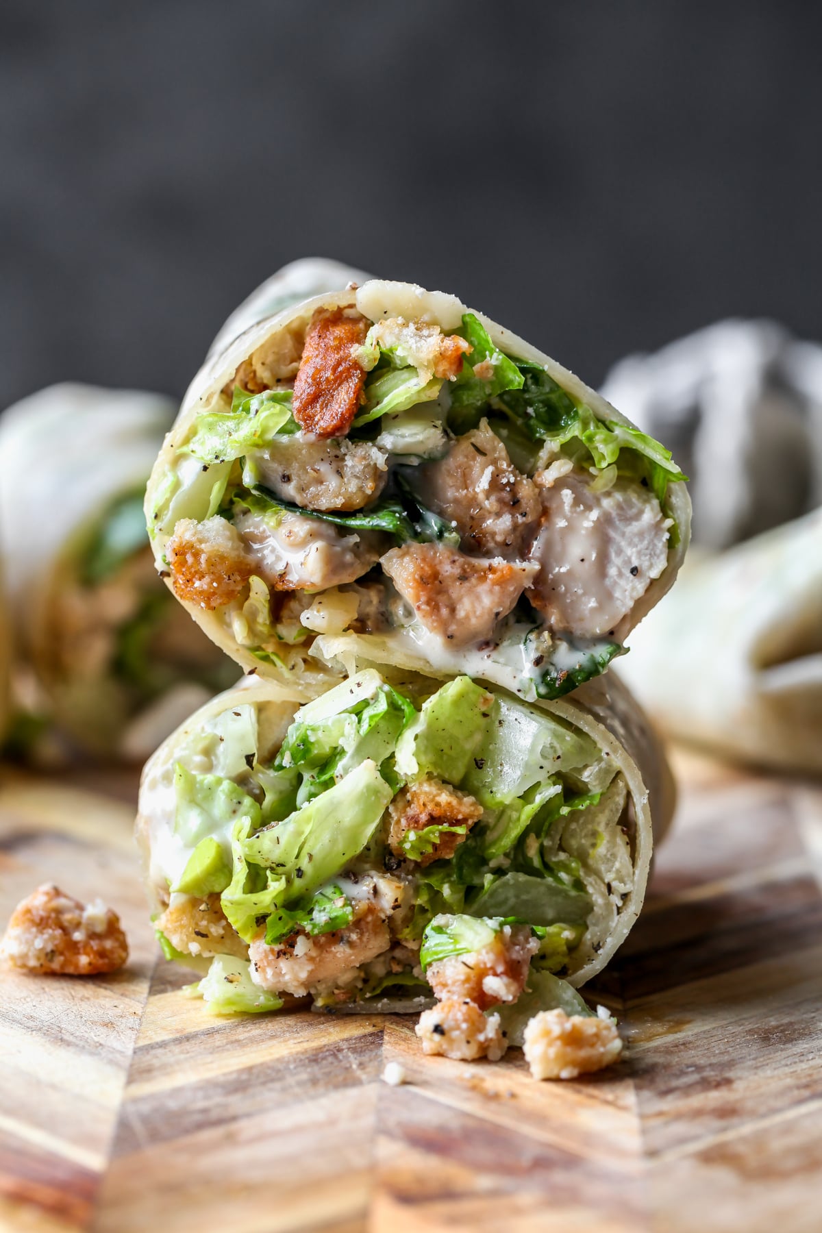 A Miso Chicken Caesar Wraps sliced in half and stacked on top of one another on a wooden cutting board.