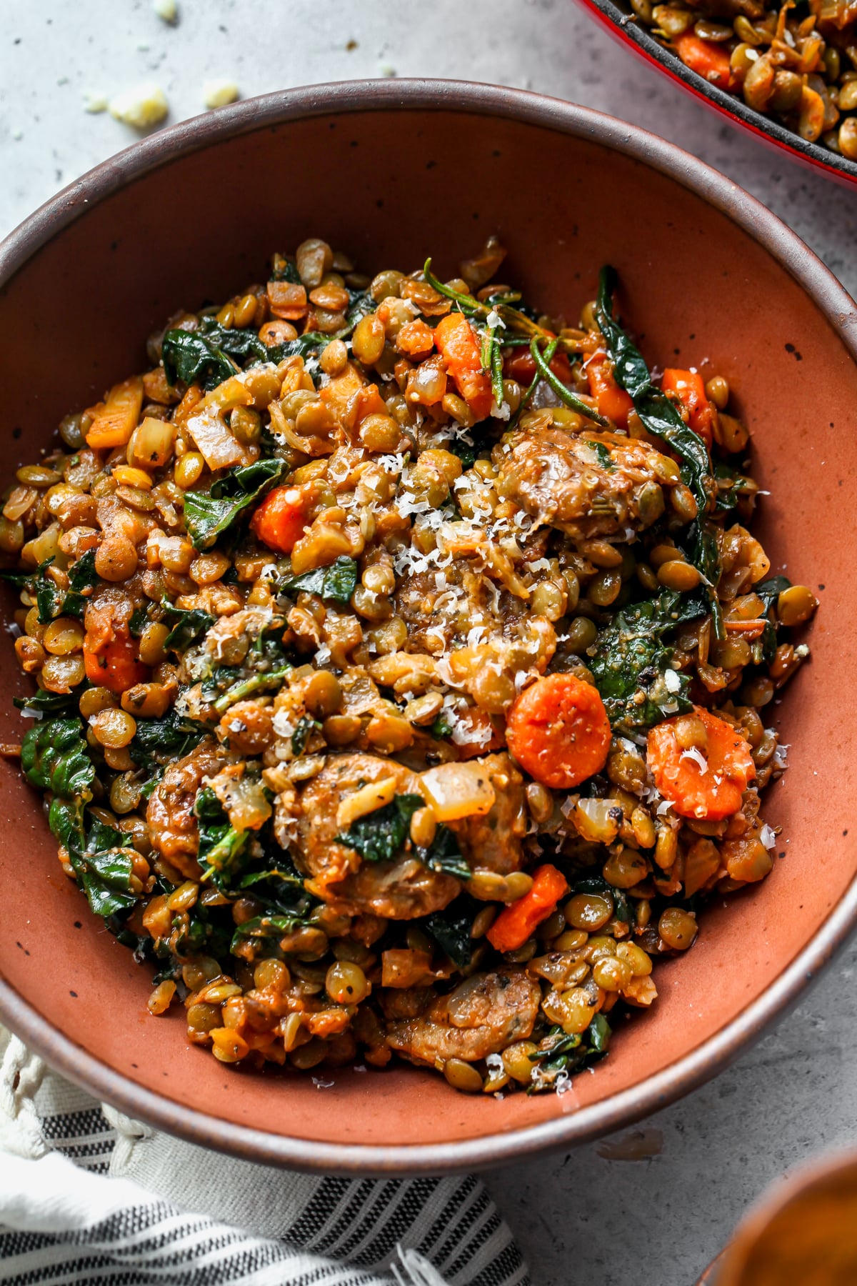 A sand-colored bowl of Tuscan sausage and lentils topped with grated cheese.