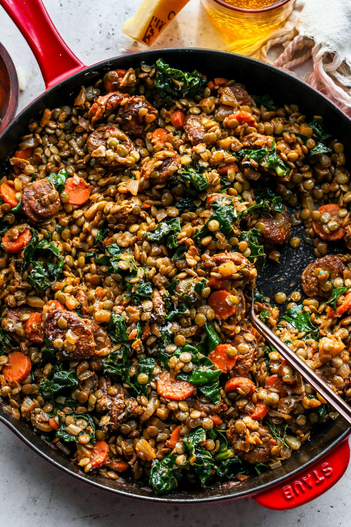 A gold serving spoon stirring into a pan of chicken sausage and lentils.