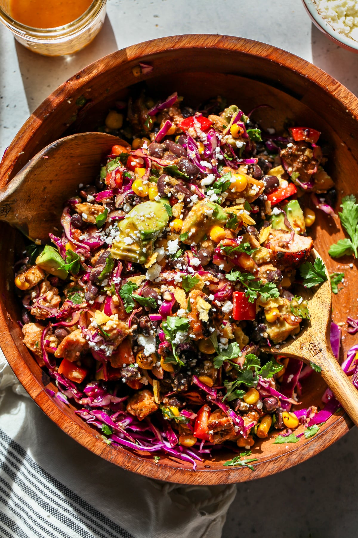 Chipotle Chicken Salad being tossed with wooden serving spoons in a large wooden serving bowl.