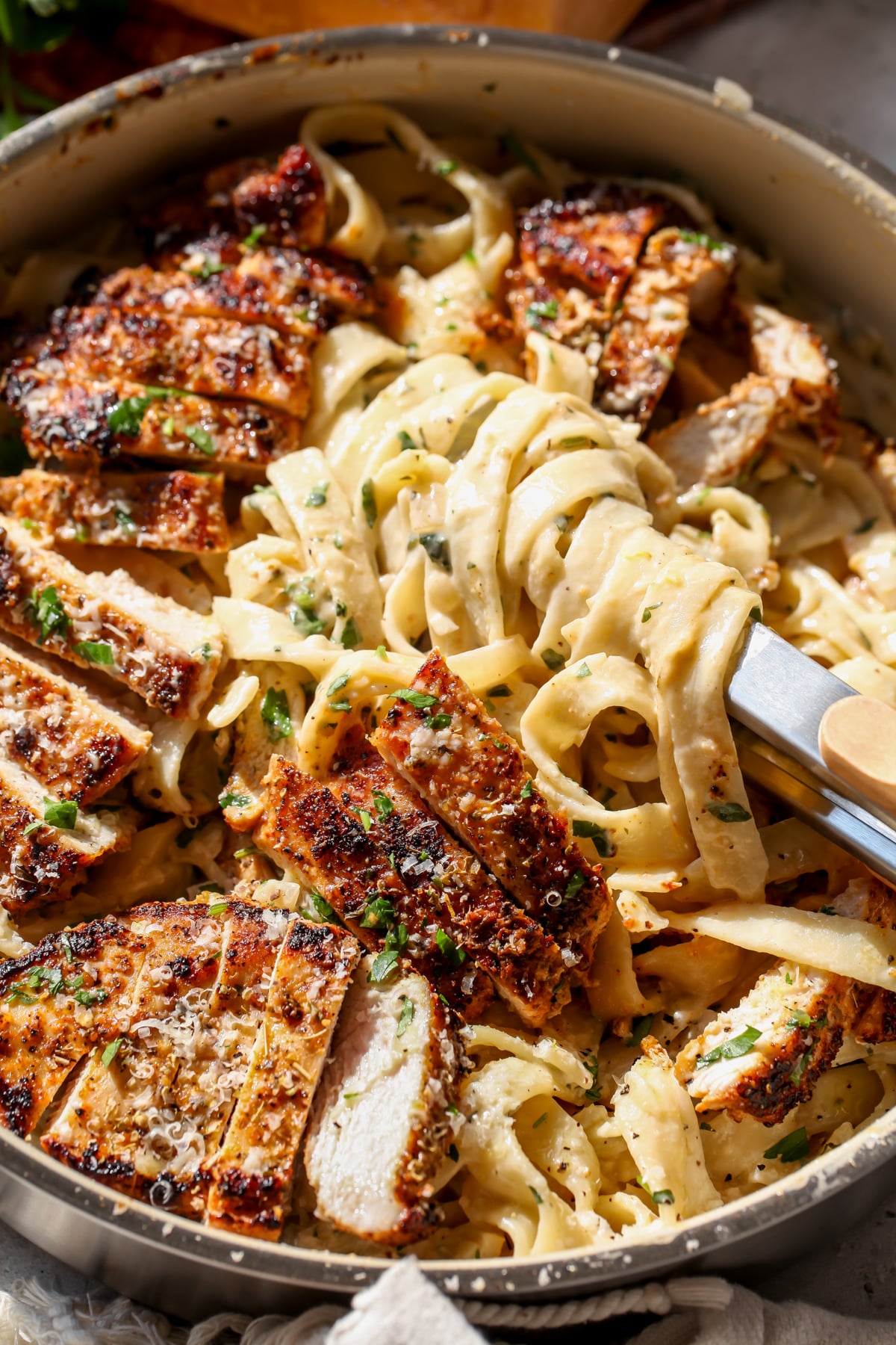 Tongs twirling a portion of creamy lemon chicken pasta in a sauté pan.