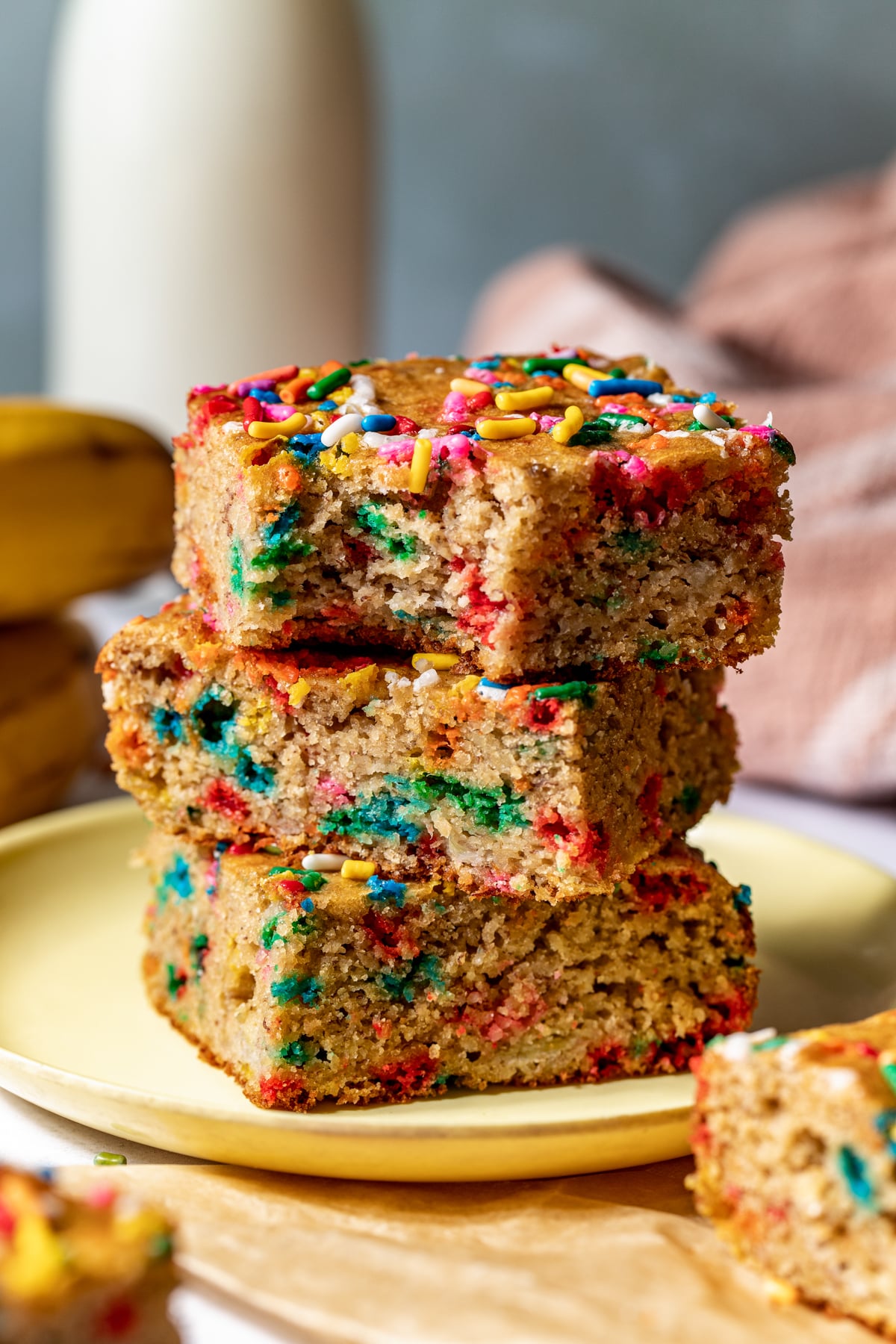 Three funfetti banana bars stacked on top of one another on a yellow plate.