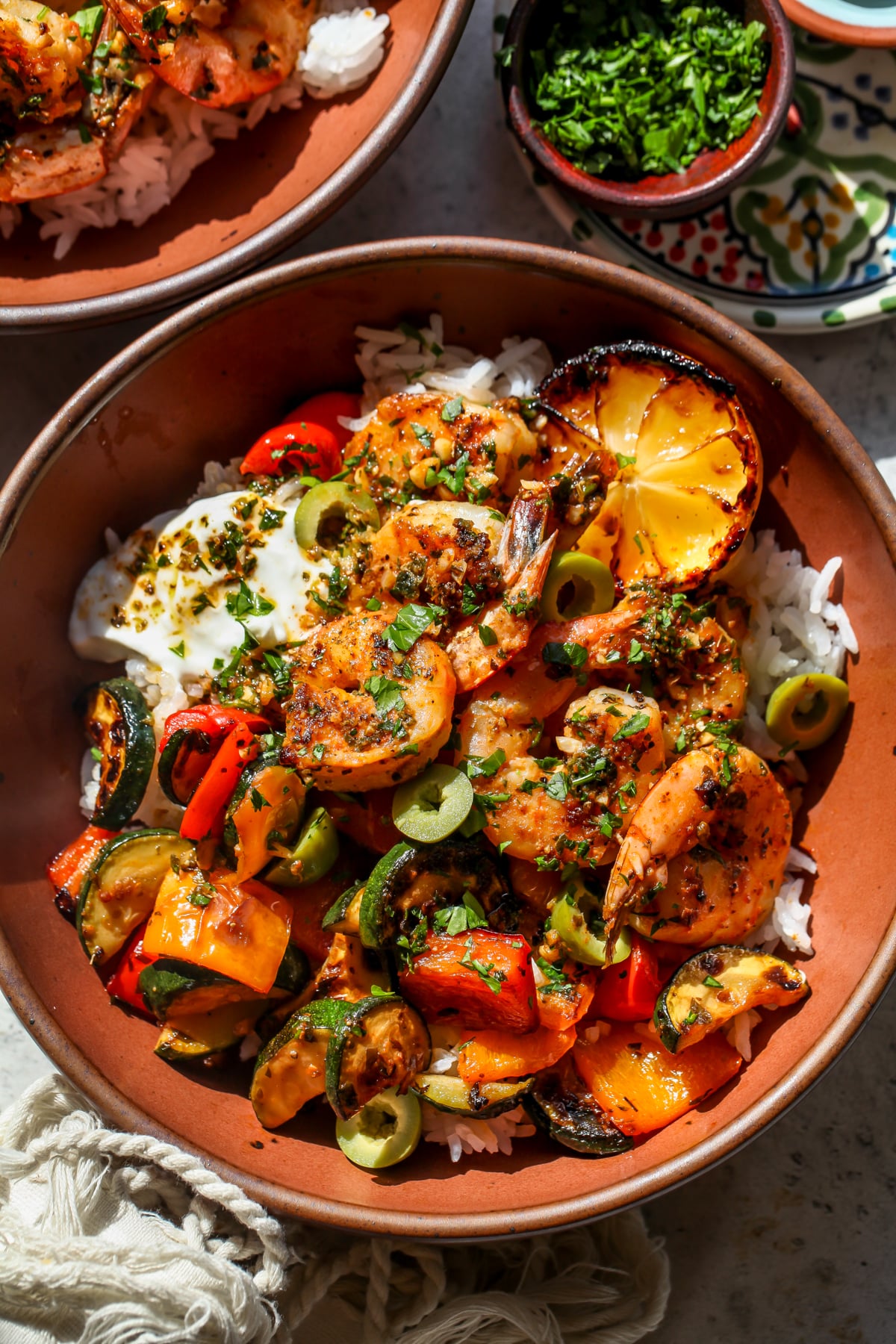 Greek shrimp bowls styled in a maroon bowl on a gray surface.