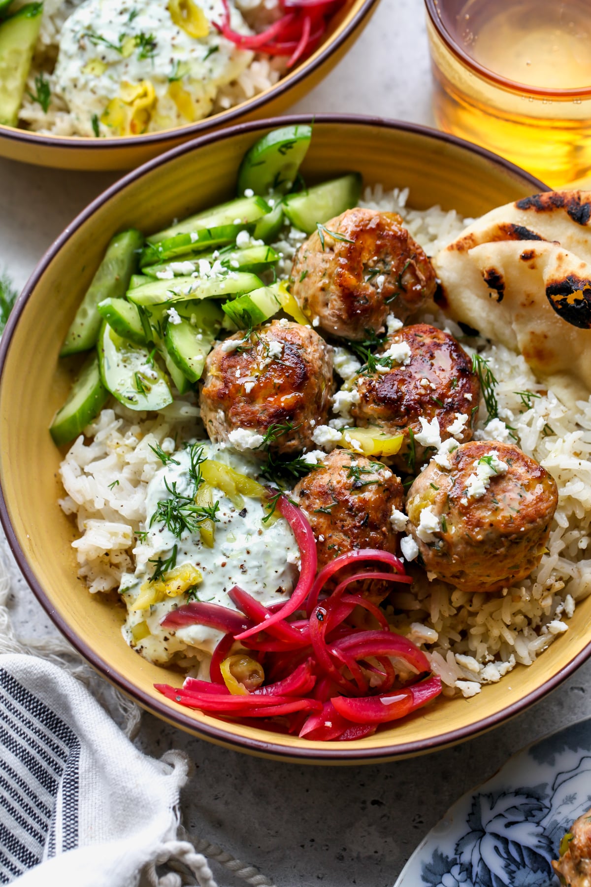 Peperoncini-Feta Turkey Meatballs styled over garlic za'atar rice in a yellow bowl with garnishes.