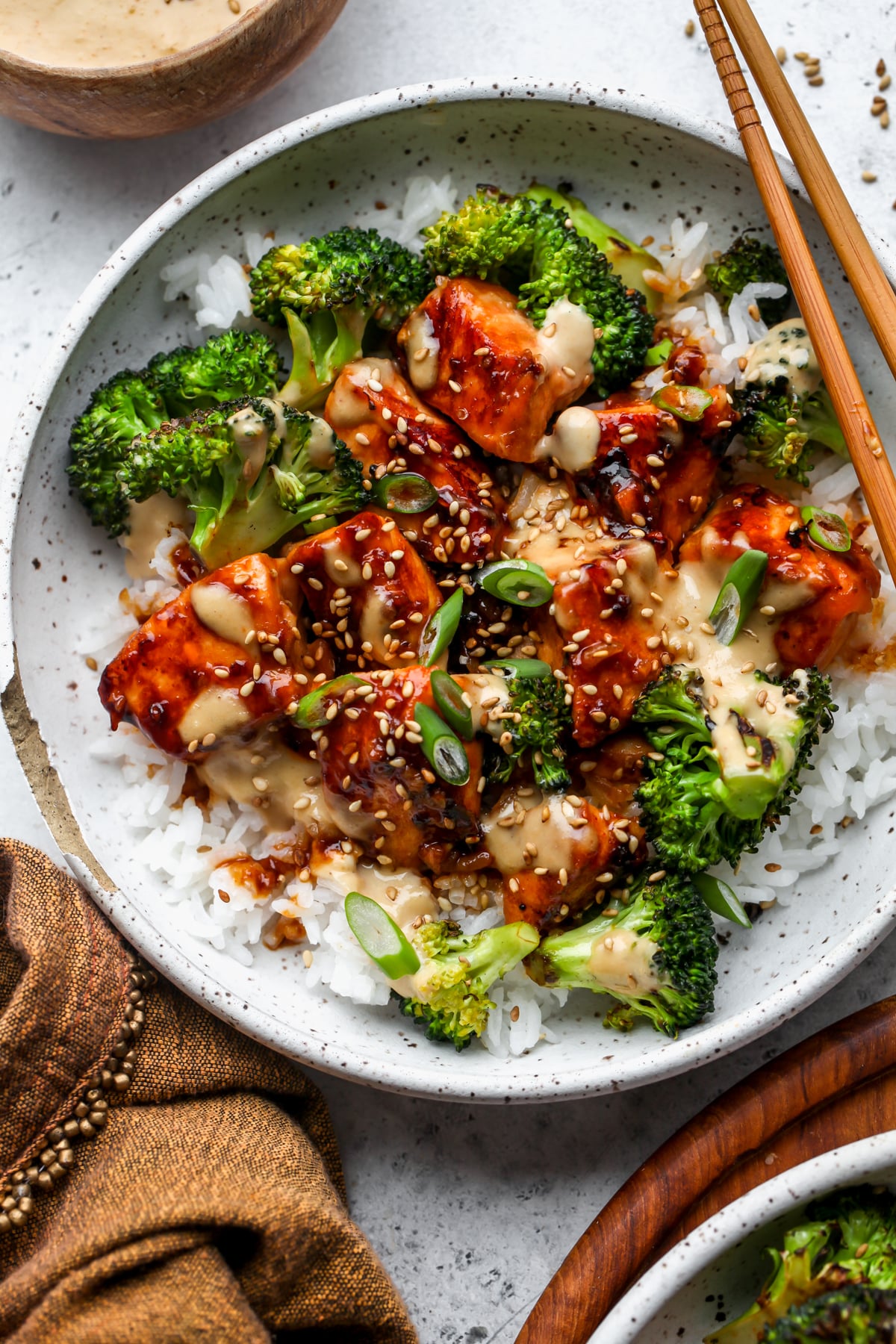 Salmon rice bowl with broccoli florets drizzled with creamy ginger sauce in a white speckled bowl.