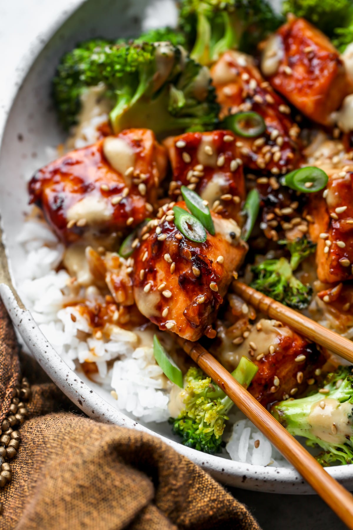 Chopsticks holding up a square of sesame glazed salmon.