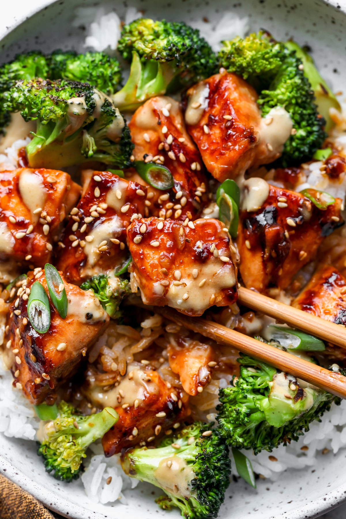 Salmon rice bowl with broccoli and ginger sauce in a white bowl with a pair of chopsticks picking up a piece of salmon.