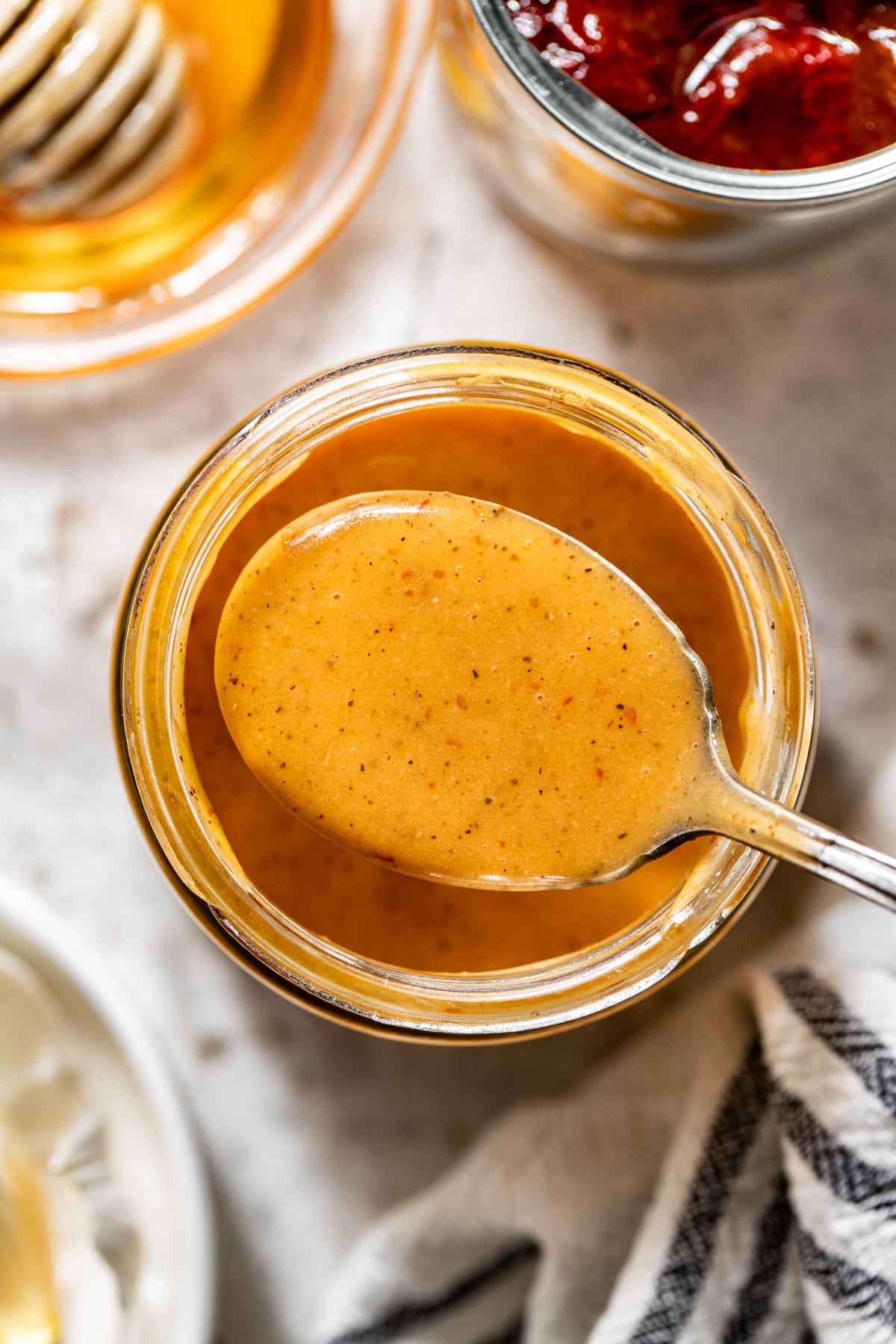 A spoon showing a portion of chipotle honey vinaigrette in a jar.