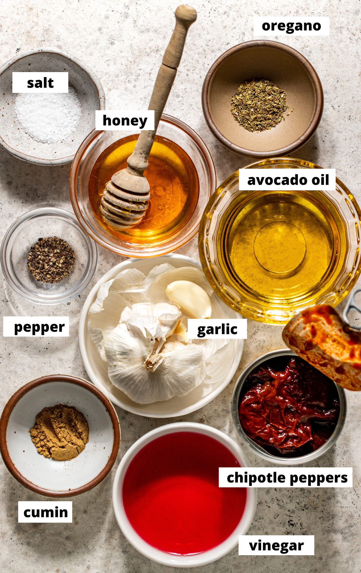 Recipe ingredients in separate bowls and jars arranged on a textured surface with labels.