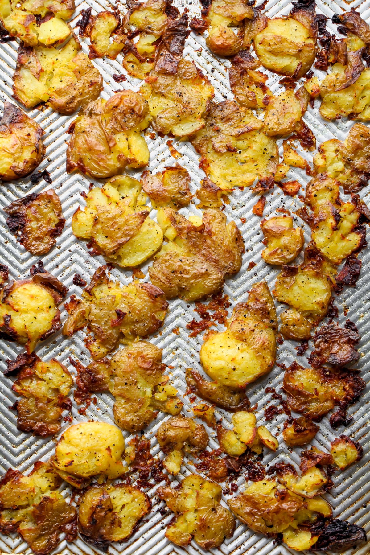 Crispy smashed potatoes arranged on a large rimmed baking sheet.
